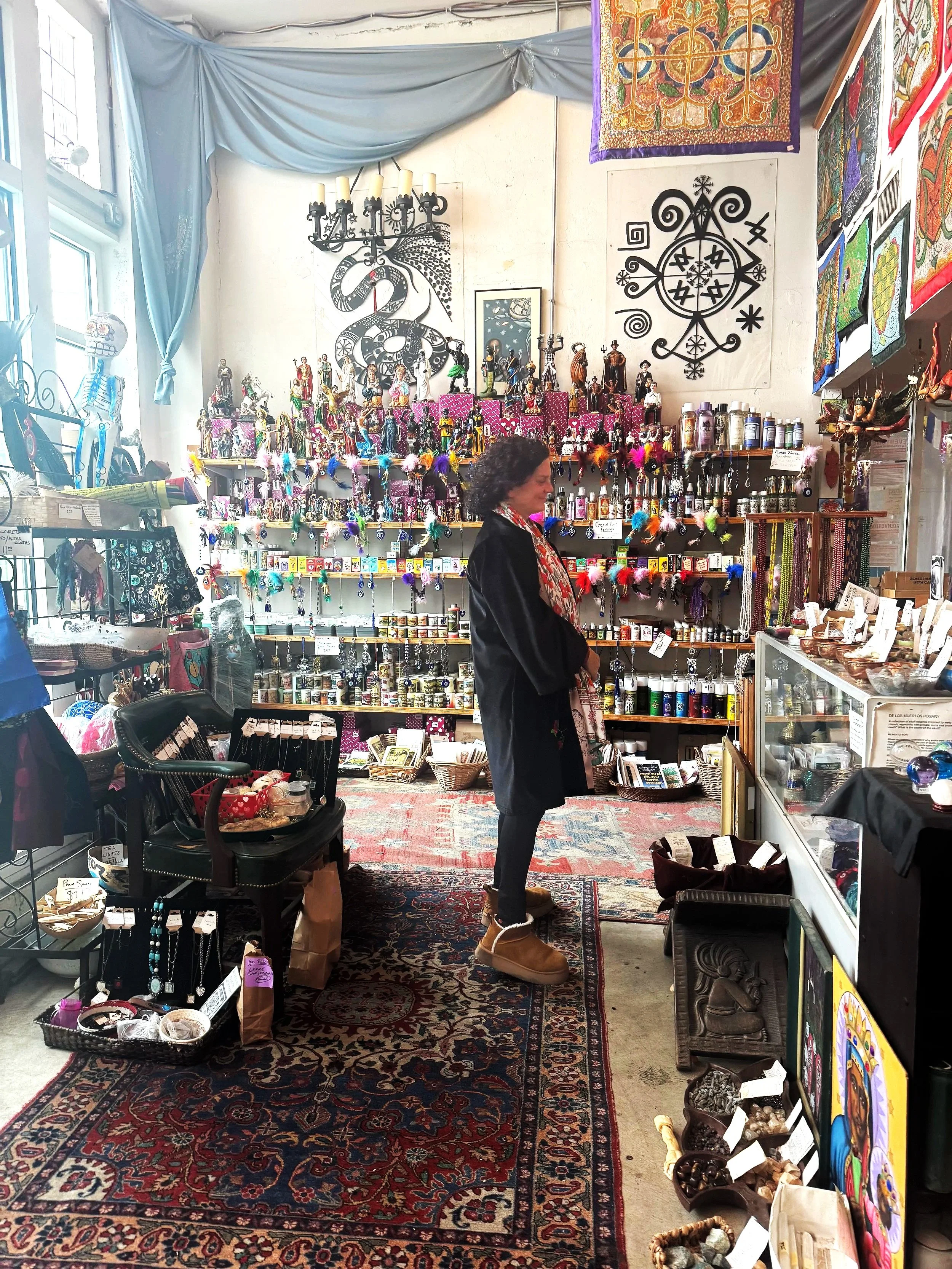 Interior of a Botanica shop in New Orleans on an excursion during Seducing the Muse. A woman is browsing, wearing tan boots and a patterned scarf.