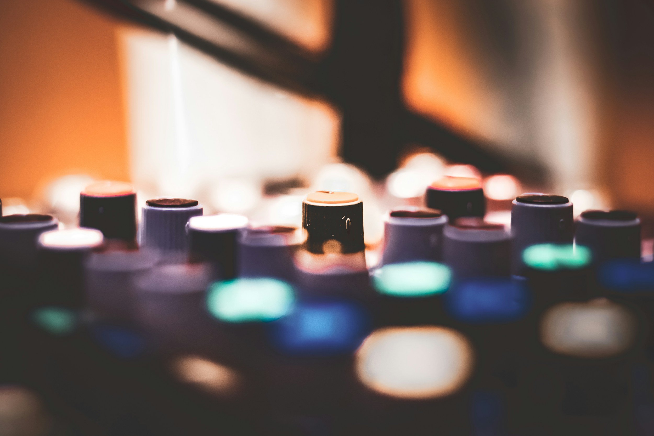 Close-up of colorful DJ mixing console knobs and buttons, with a blurred background.