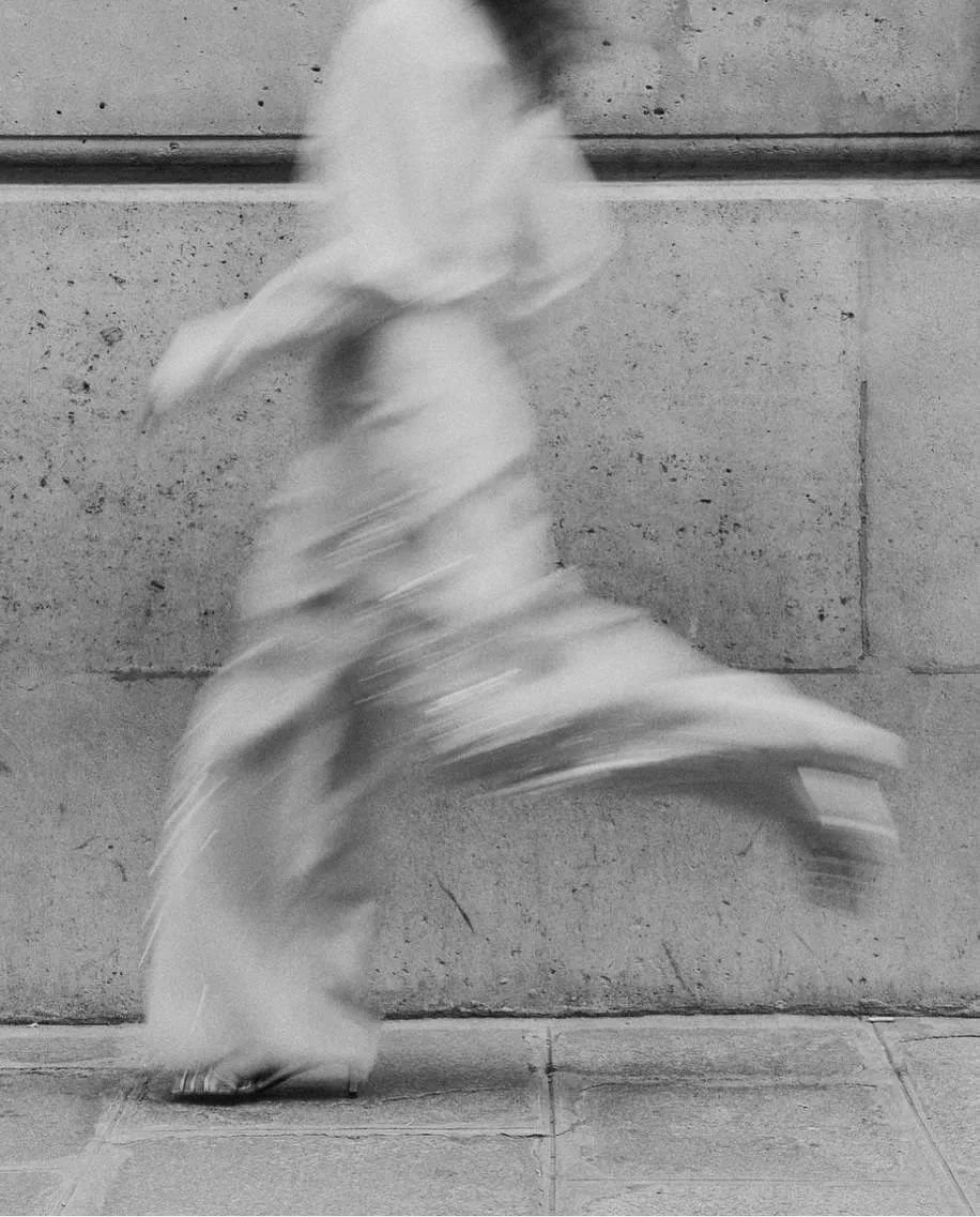 A blurred person walking on a sidewalk against a concrete wall.