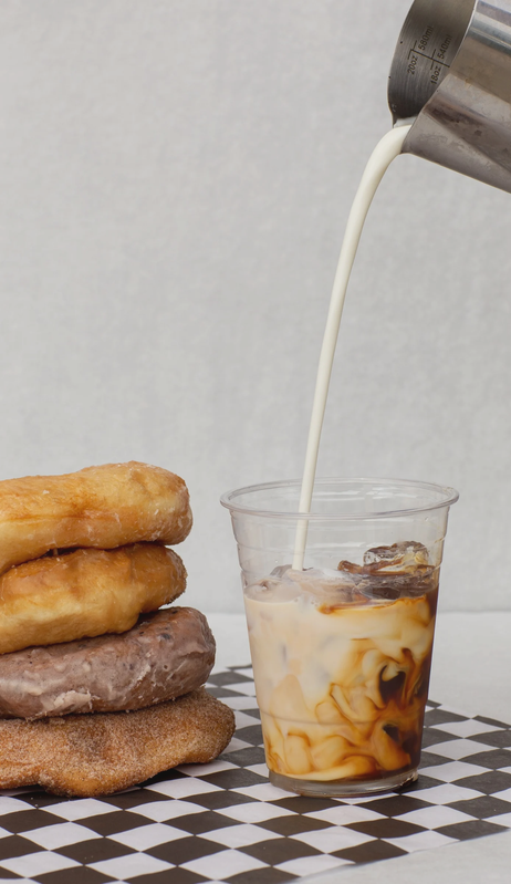 Pouring milk into iced coffee with ice cubes, next to a stack of fried chicken fillets on checkered paper.