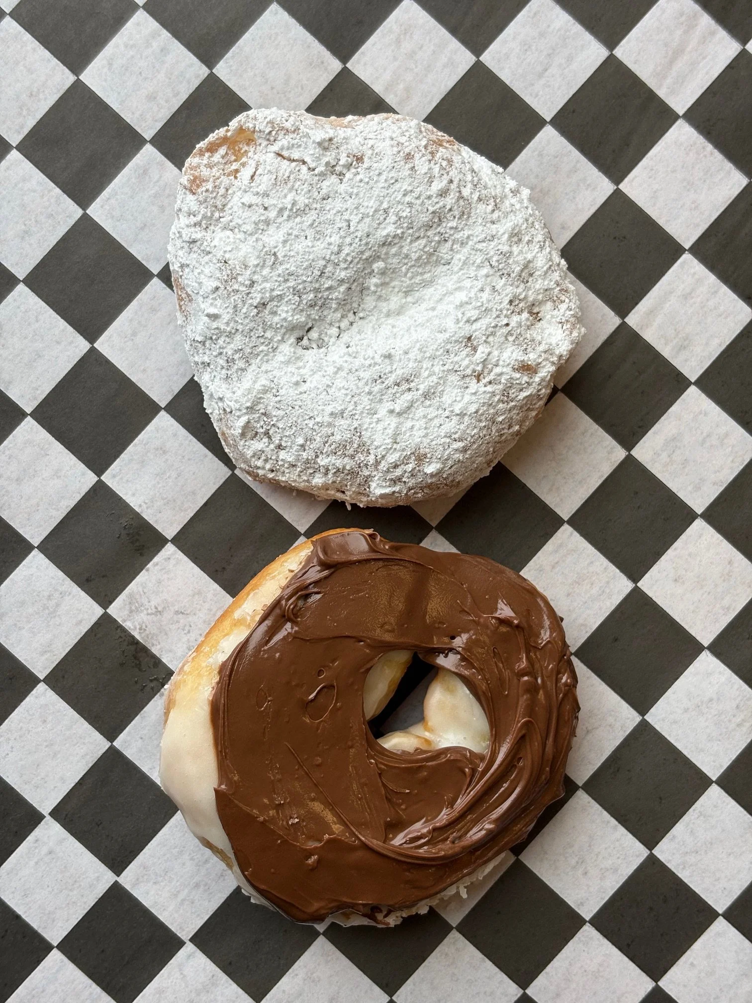 A powdered sugar-covered cookie and a chocolate and vanilla frosted doughnut on black and white checkered paper.