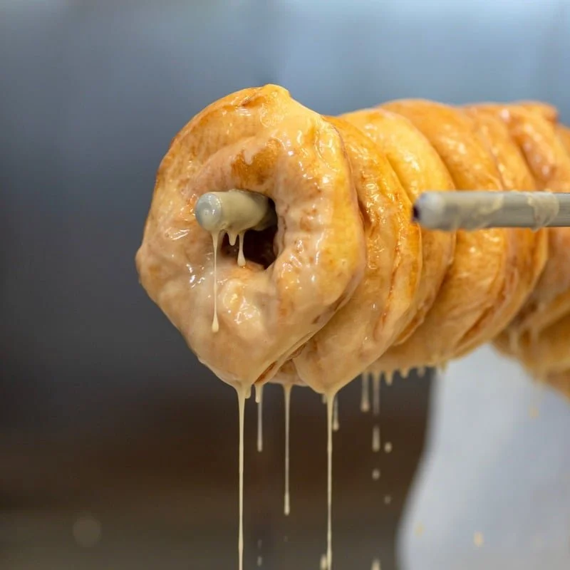 Close-up of a large, syrup-dripping cinnamon roll on a skewer.