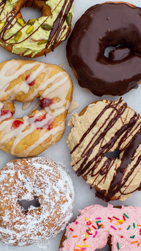 Six assorted donuts with various toppings and glazes, including chocolate, icing and sprinkles.