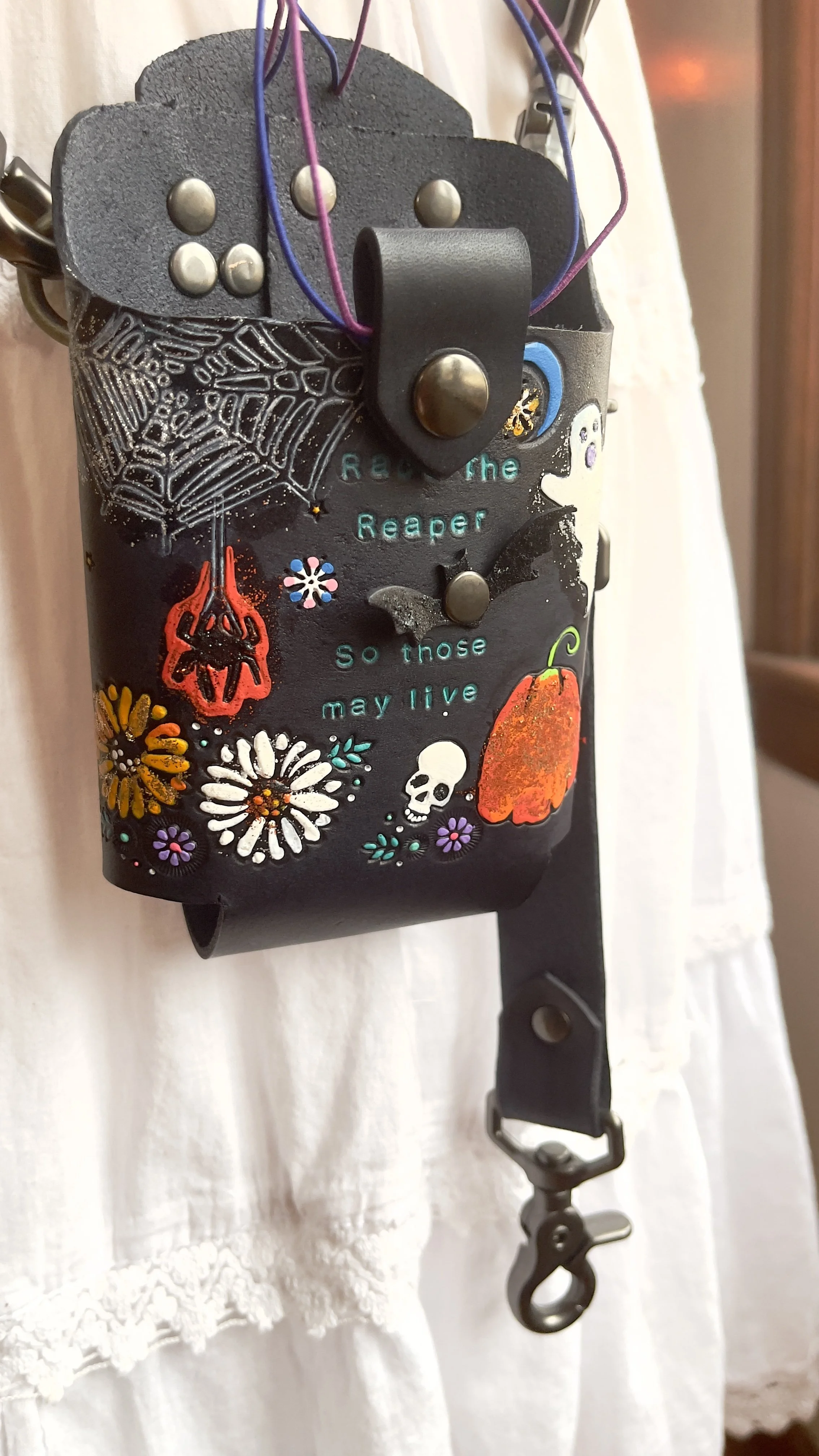 a black leather fire radio bucket with fun halloween designs tooled on it. They include spiders, skulls, pumpkins and autumn flowers. It has silver hardware and a thick elastic retaining strap