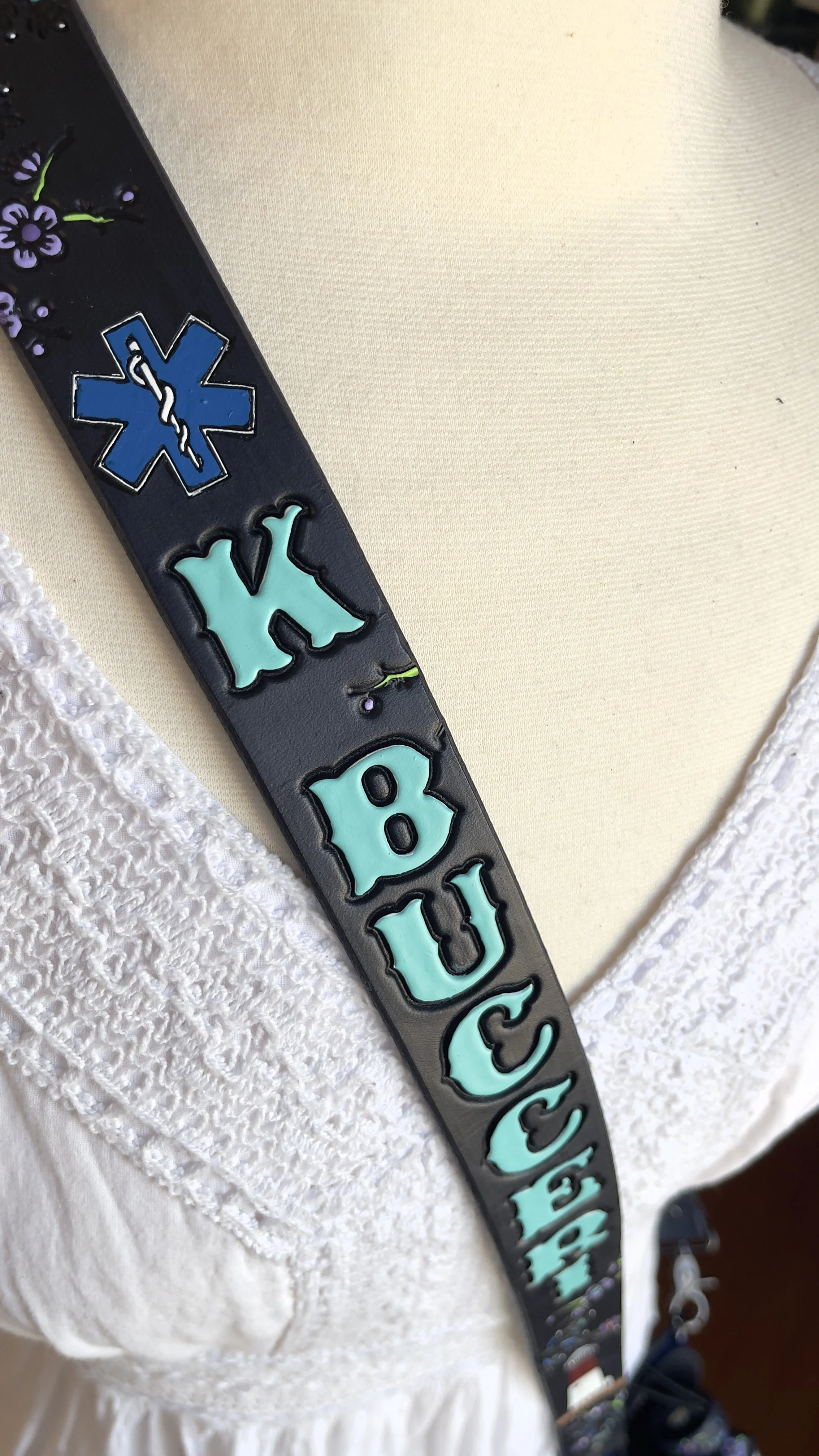 a black leather fire radio strap with a handpainted EMS star of life above the customers name. The name has been stamped and painted in a bright teal.