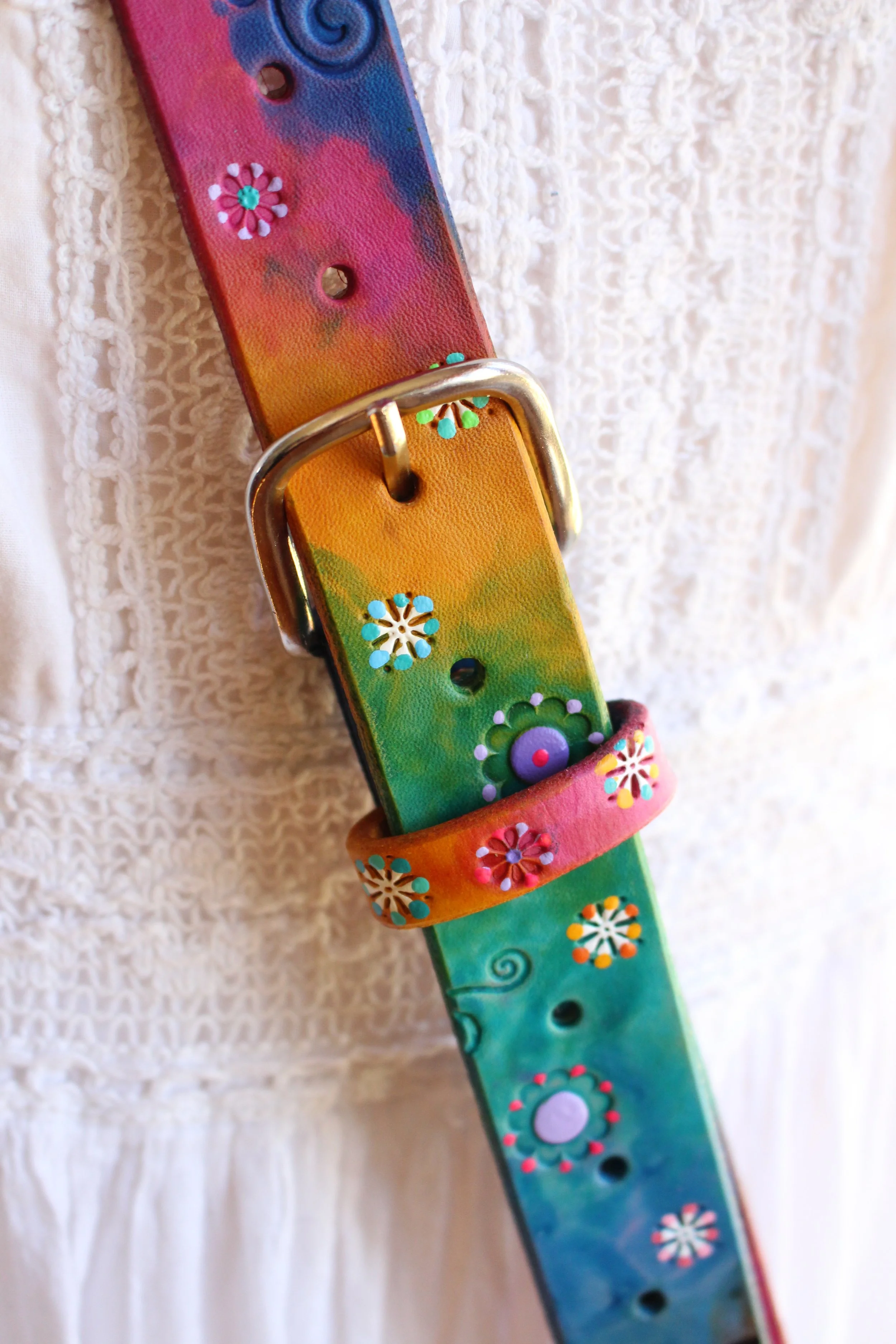 a heavy duty, thick leather crossbody fire radio strap in a rainbow stain effect using blue, gree, yellow and pinks. Hand tooled stars, flowers and dots are painted along the strap