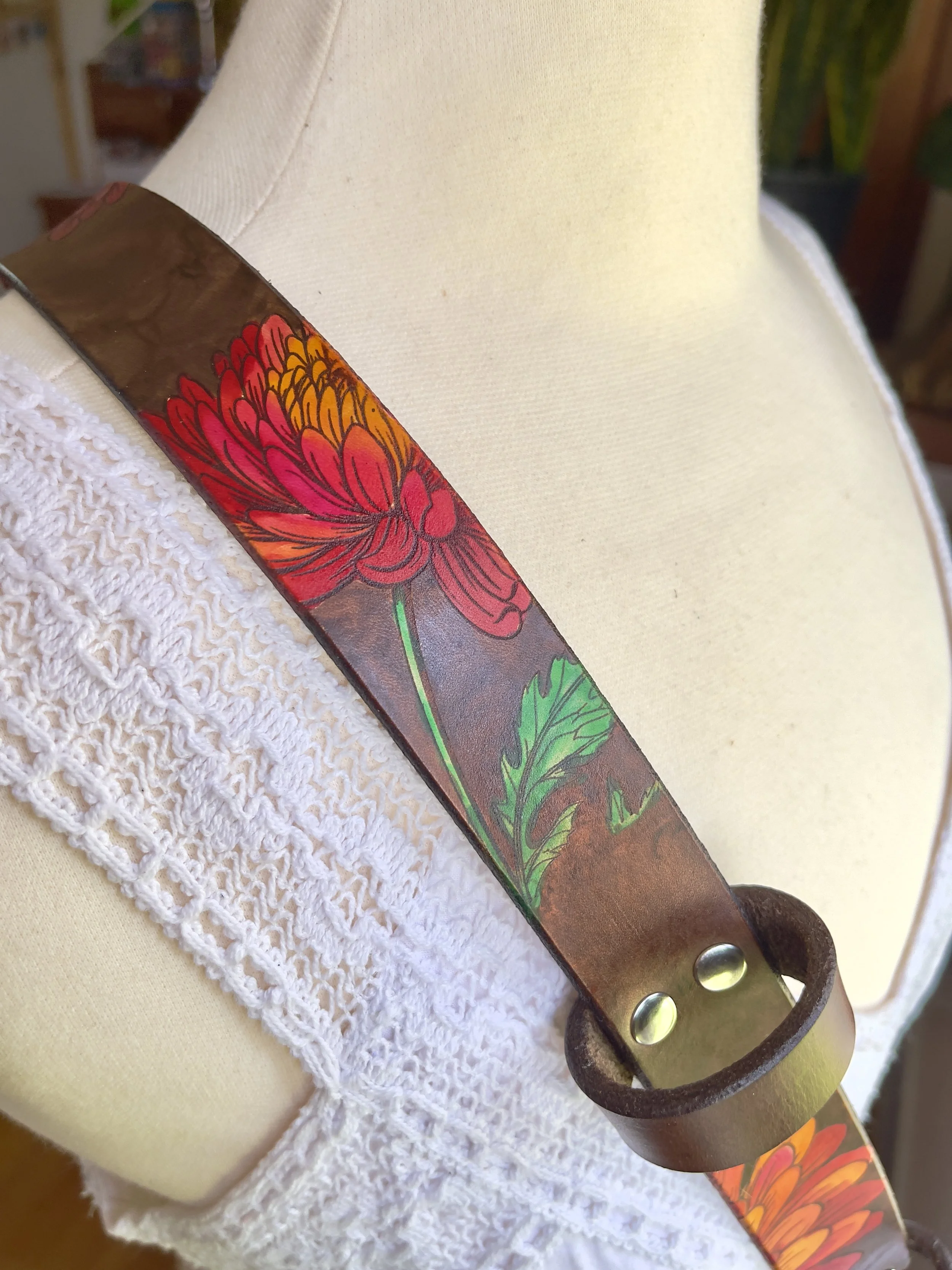 a brown crossbody leather fire radio strap with painted green leaves engraved into the leather. Hints of rosy painted chrysanthemum Flowers are seen