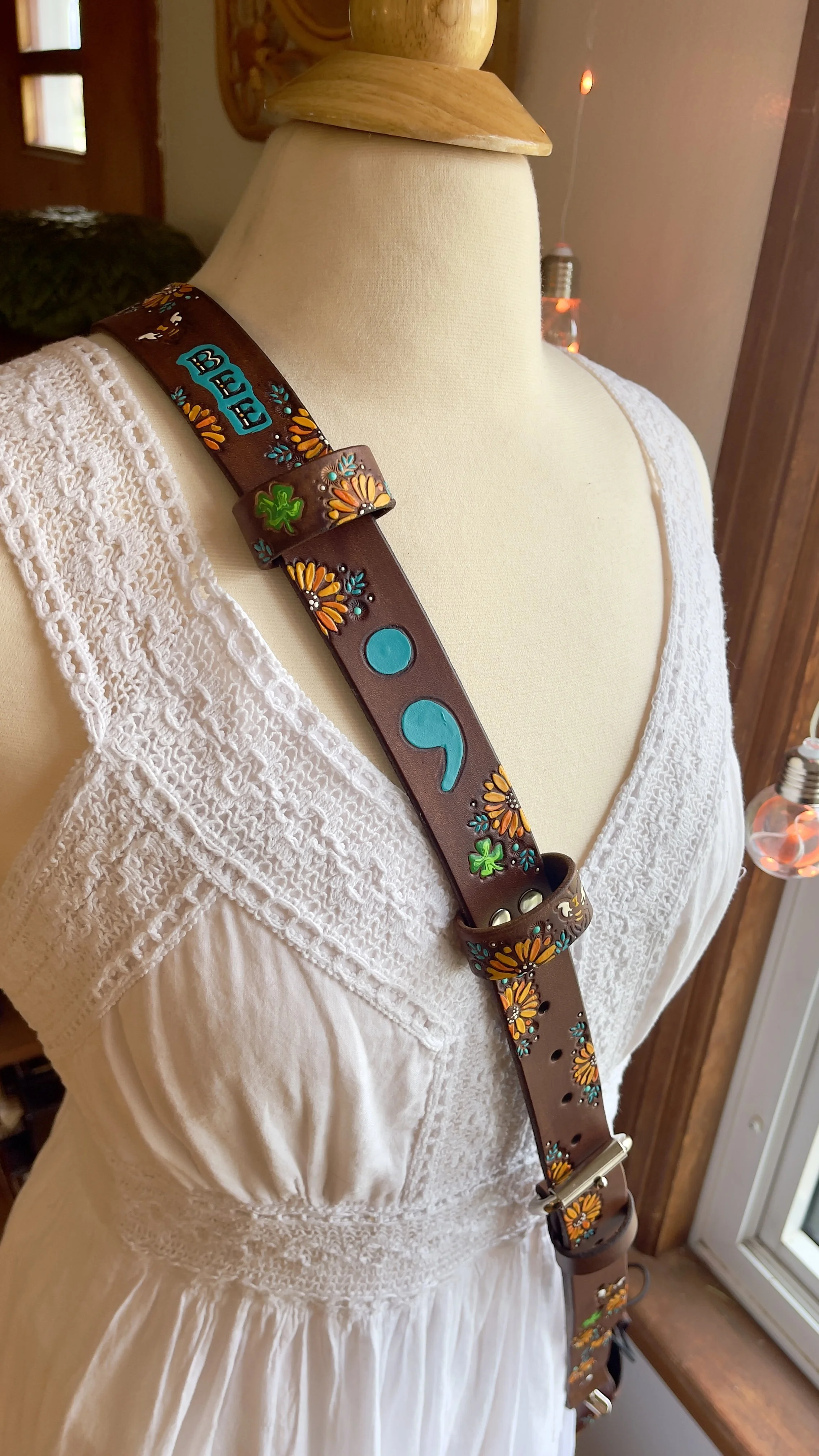 A brown leather fire radio holster covered in tooled four leaf clovers, sunflowers and a teal painted semi-colon