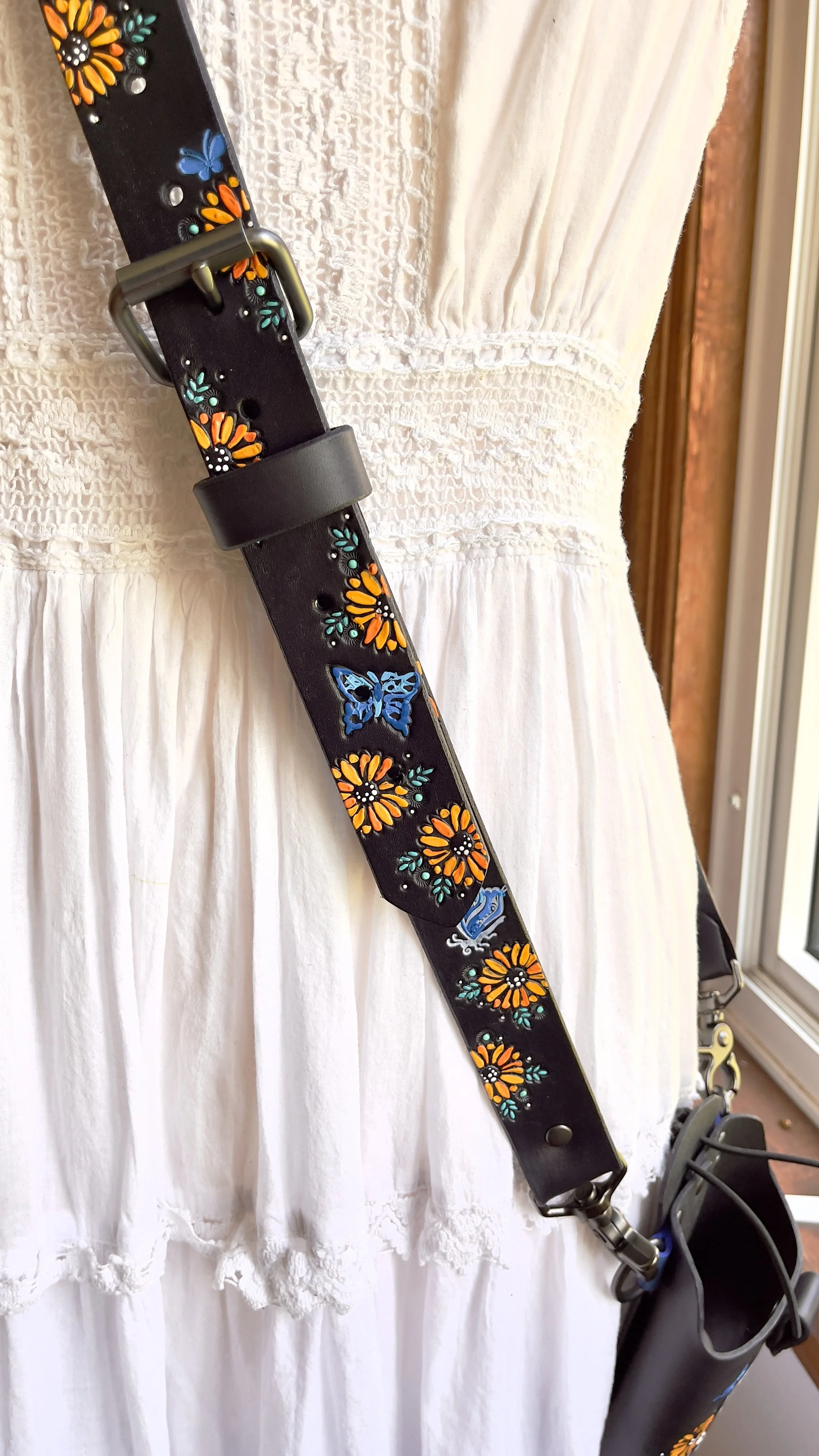 A crossbody black leather fire radio strap covered in hand tooled sunflowers, blue butterflies and white accents.