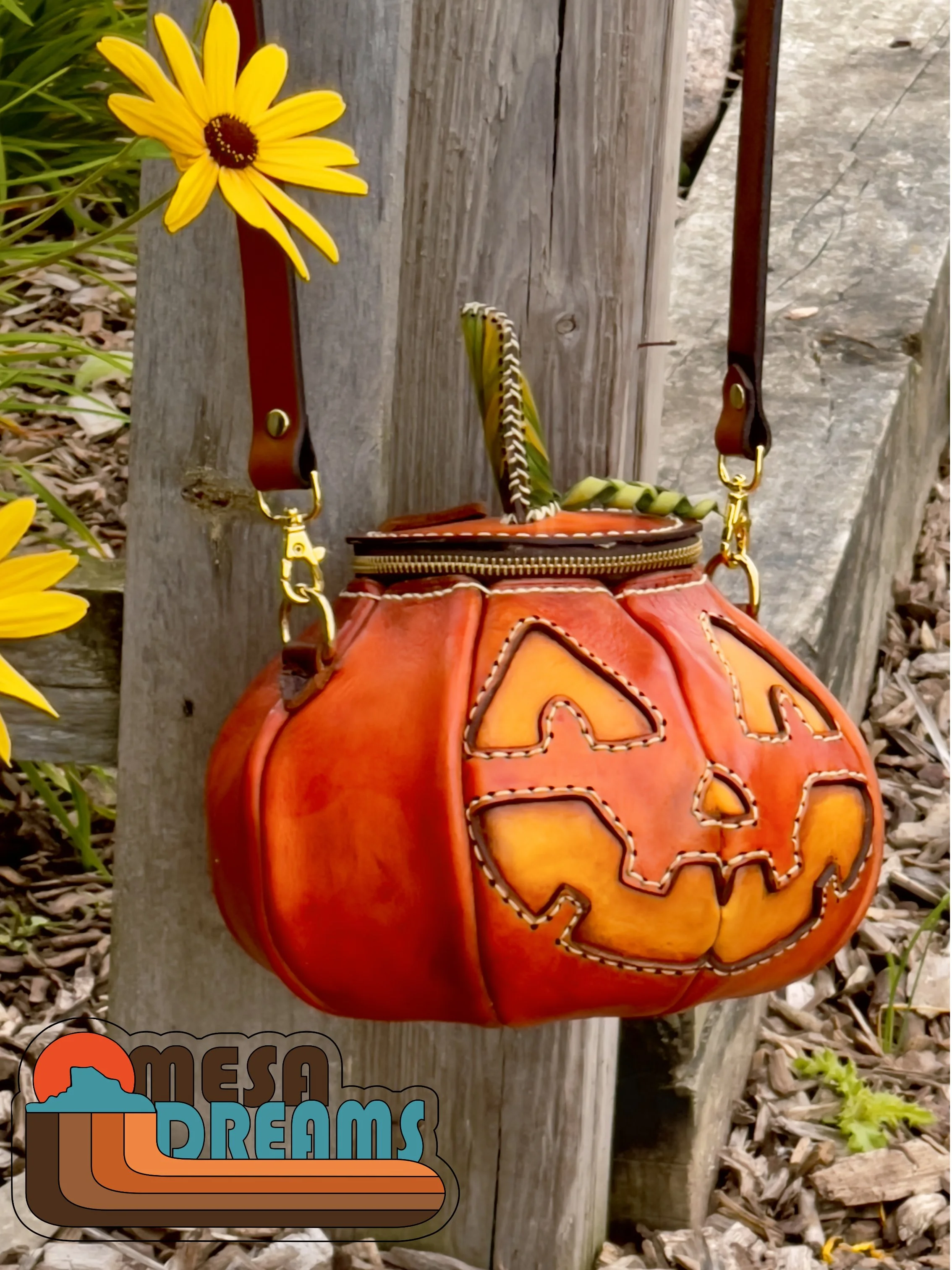 The Great Pumpkin leather bag hanging on a weathered wooden fence post in a meadow