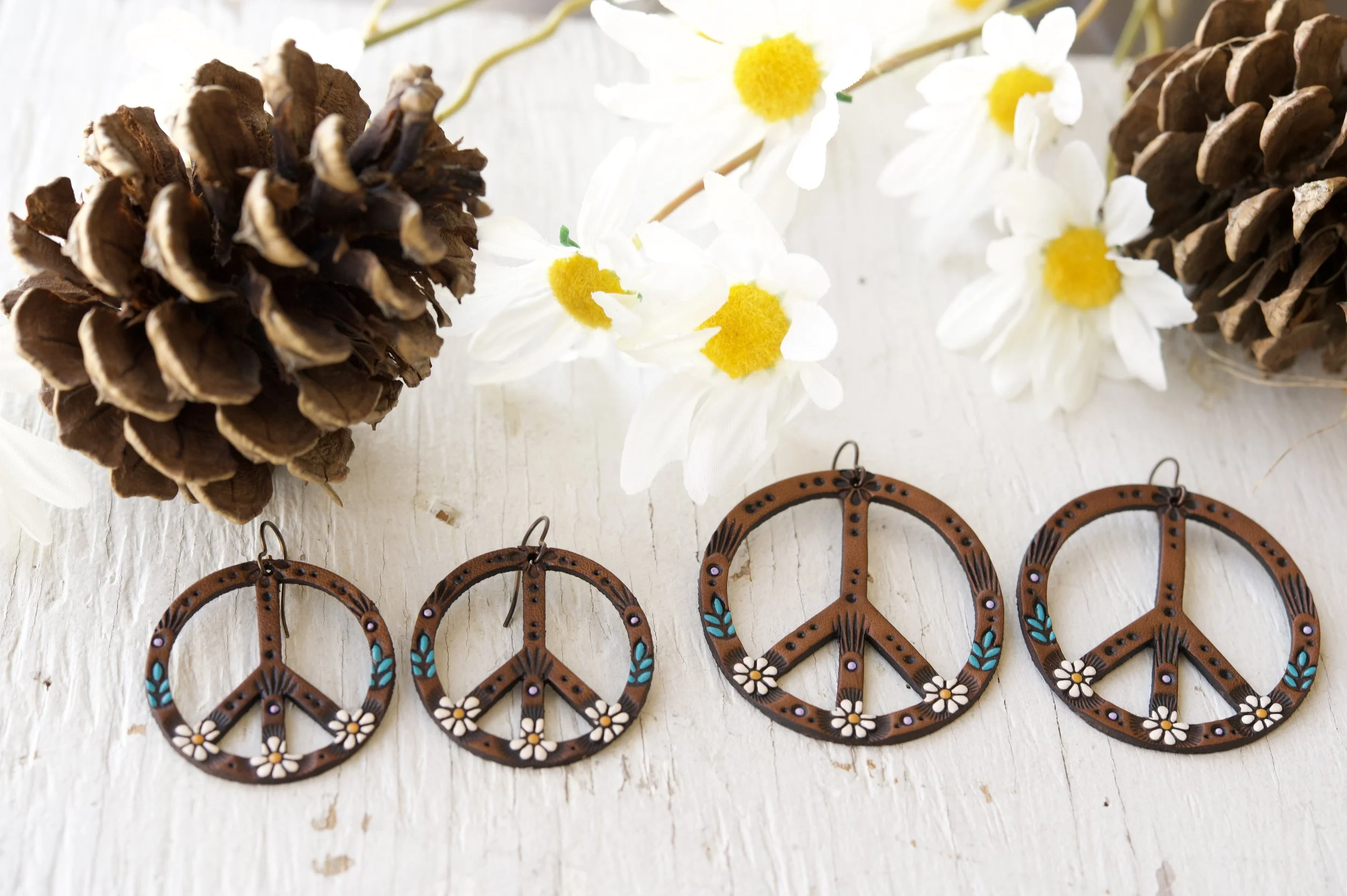 an image showing the 1.5” and 2” versions of the classic Daisy peace sign earrings side by side on a rustic white background