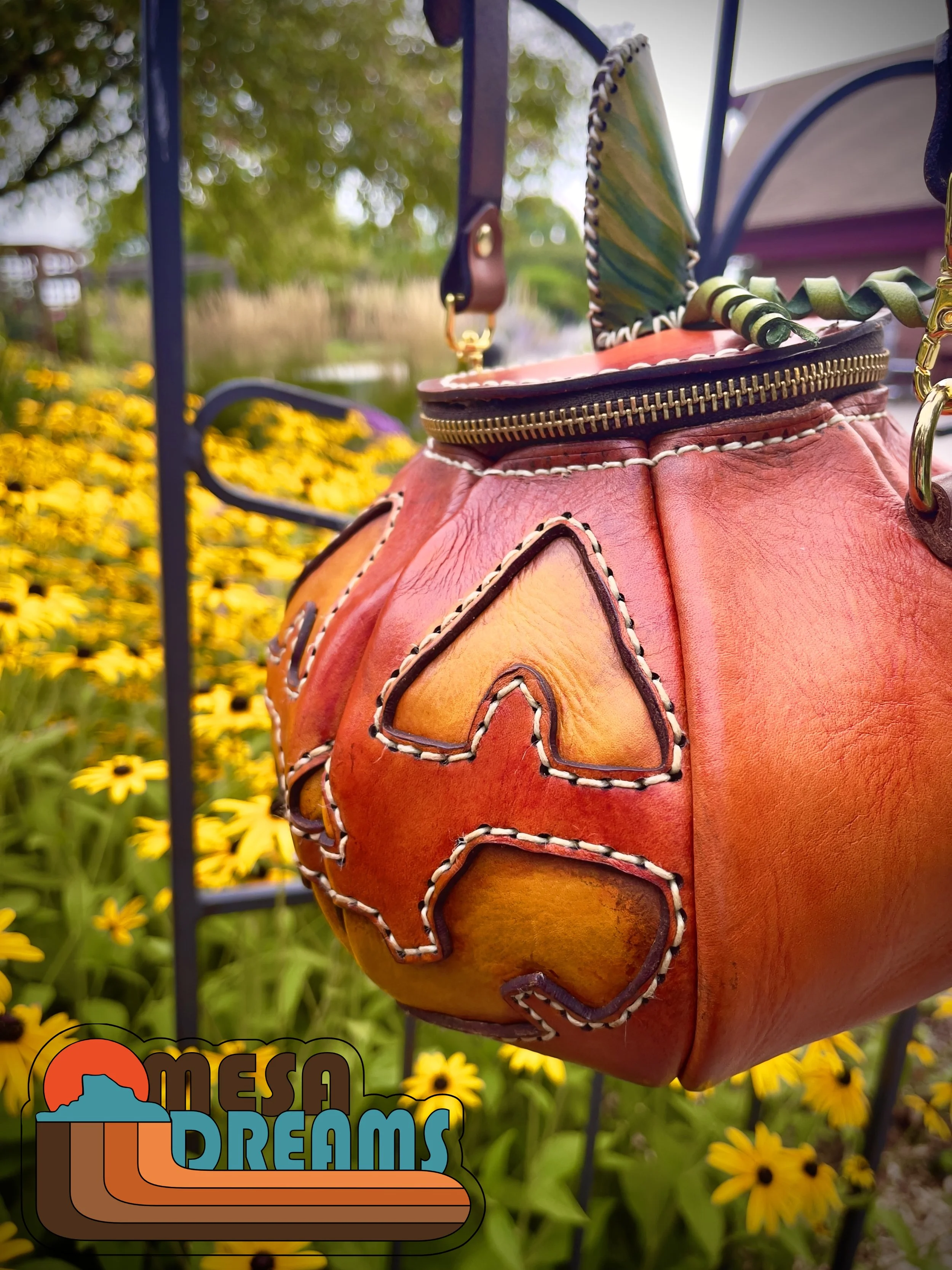 The Great Pumpkin bag hanging in profile in a garden of yellow black-eyed Susan flowers. The bag is hanging from a wrought iron archway