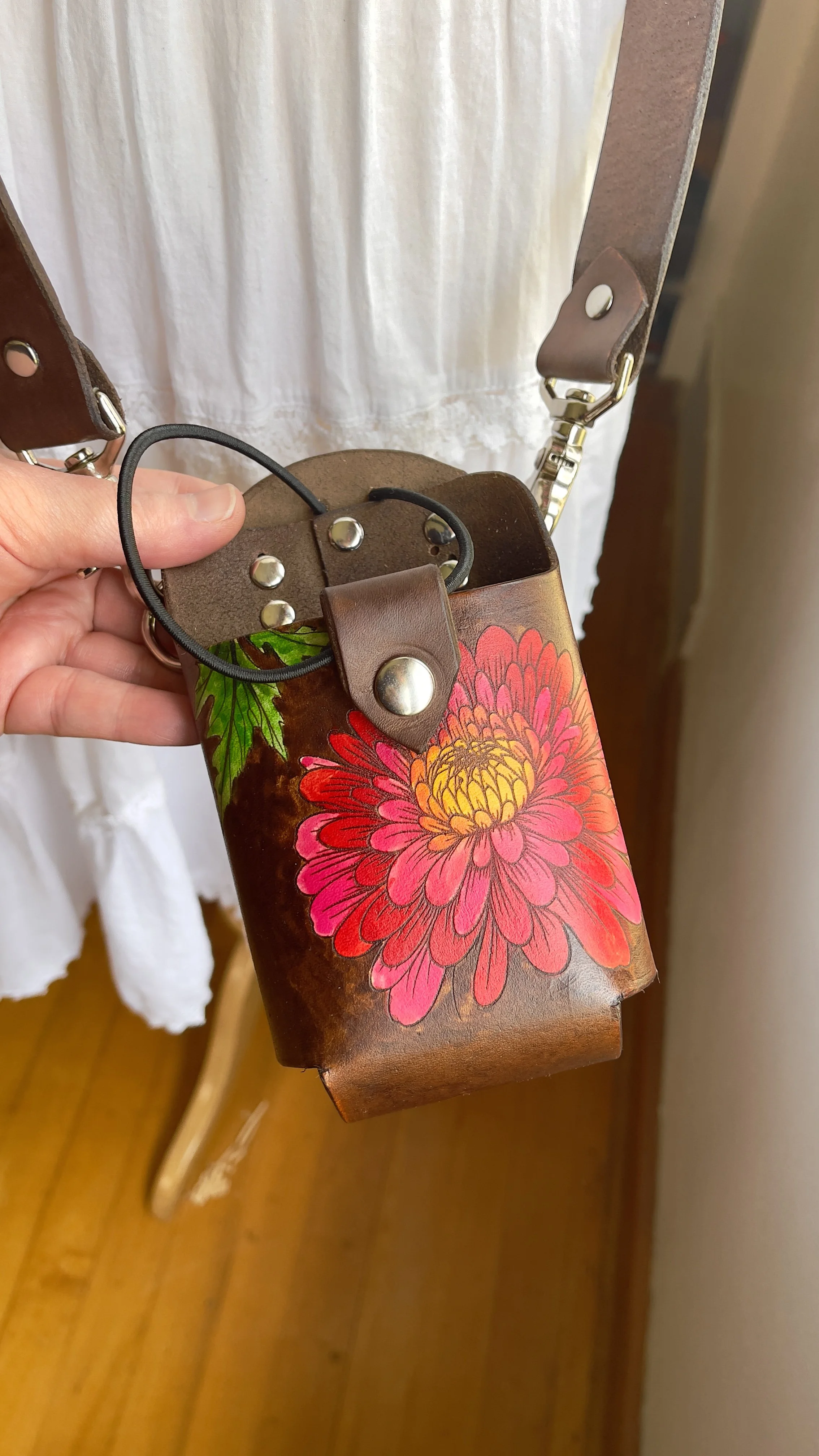 a brown leather fire radio holster adorned with an engraved chrysanthemum flower that is hand painted in red, pinks and yellows