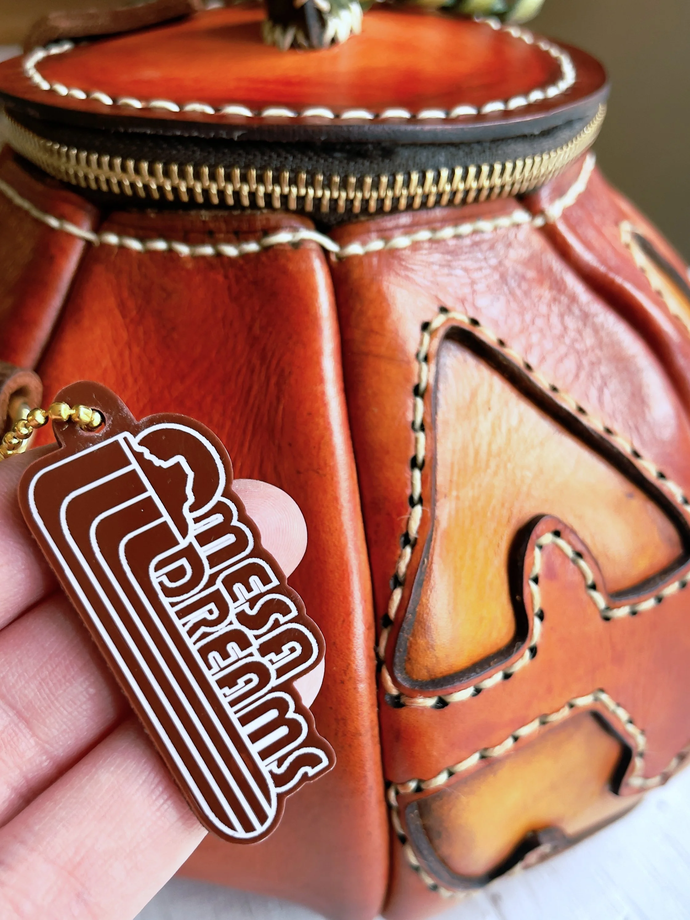 The photo is highlighting the Mesa Dreams logo bag tag that comes with each bag. It’s made from brown acrylic and hangs from a brass beaded chain