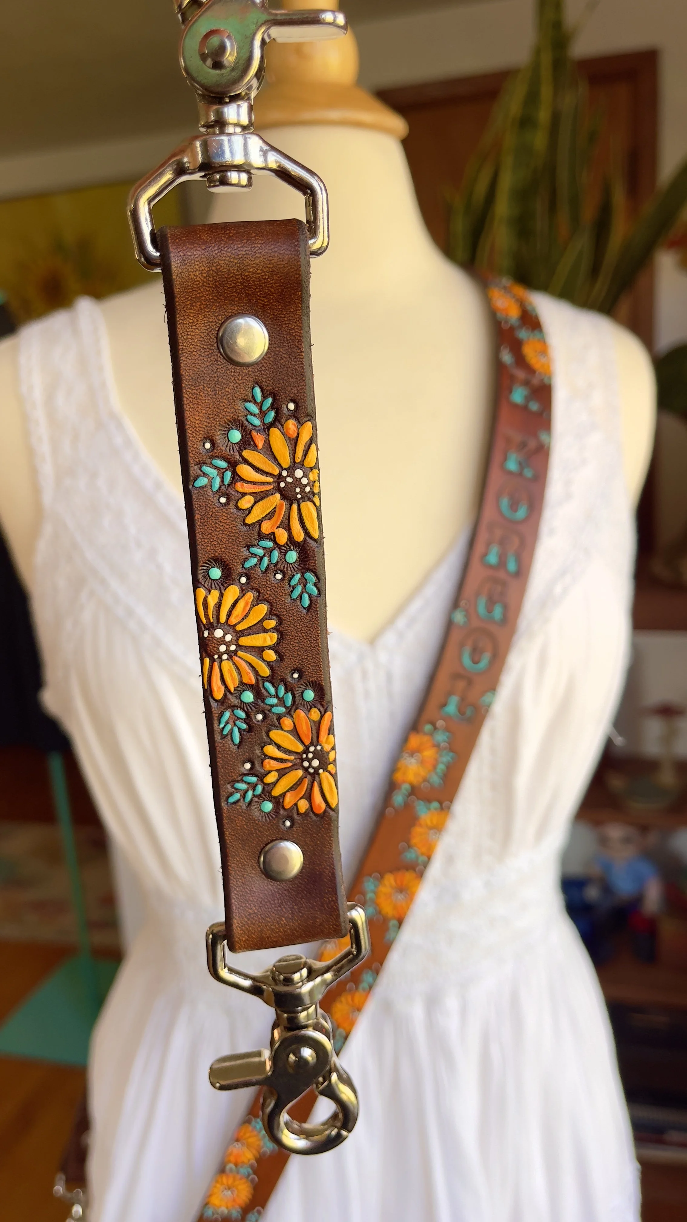 A brown leather anti-sway strap covered in vibrant yellow sunflowers and leaves with silver hardware. A crossbody fire radio strap is shown in the background in the same sunflower pattern.