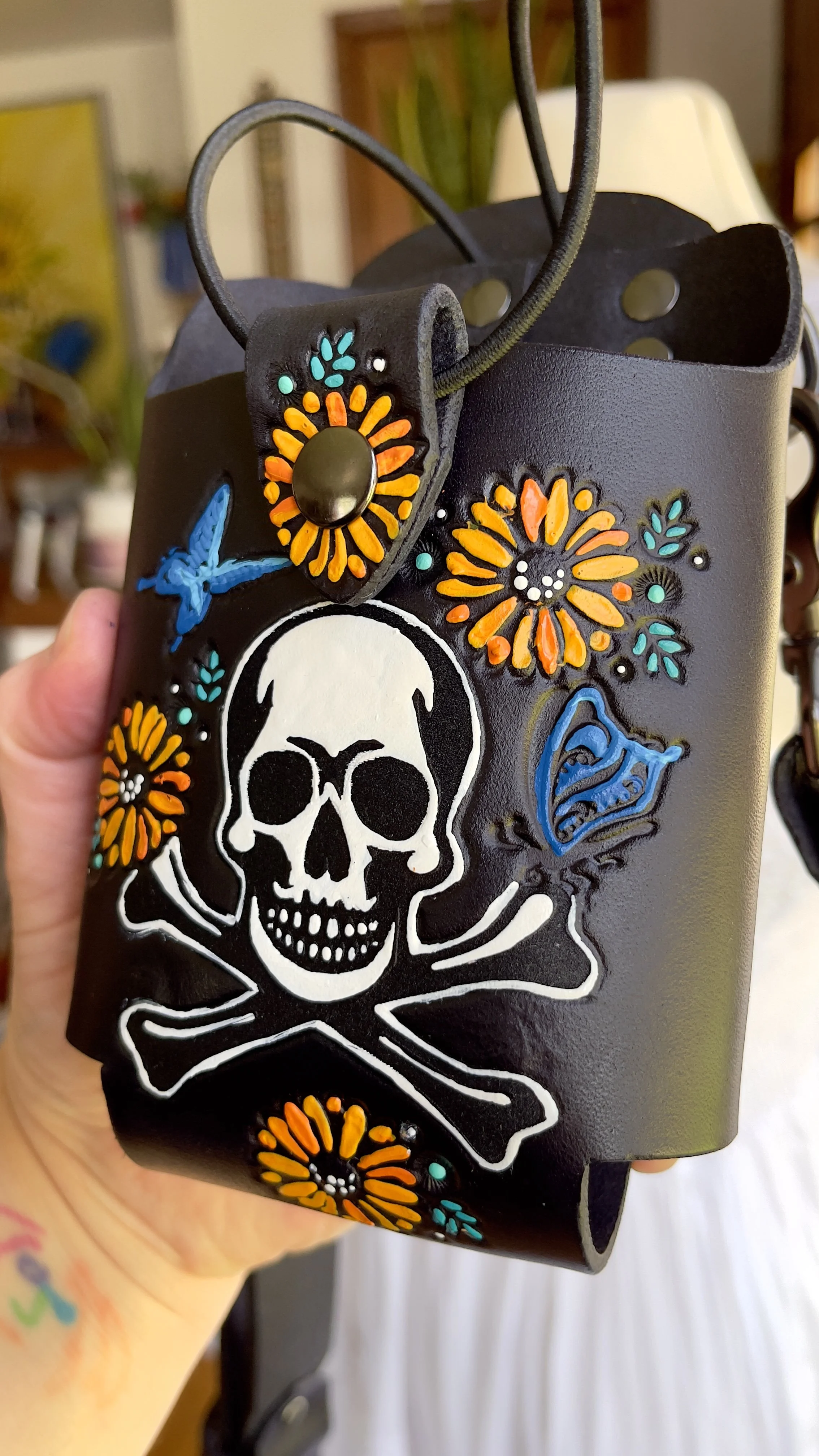 a fire radio holster adorned with a white skull and crossbones, sunflowers and blue butterflies. It has a snap closure and thick elastic retaining band
