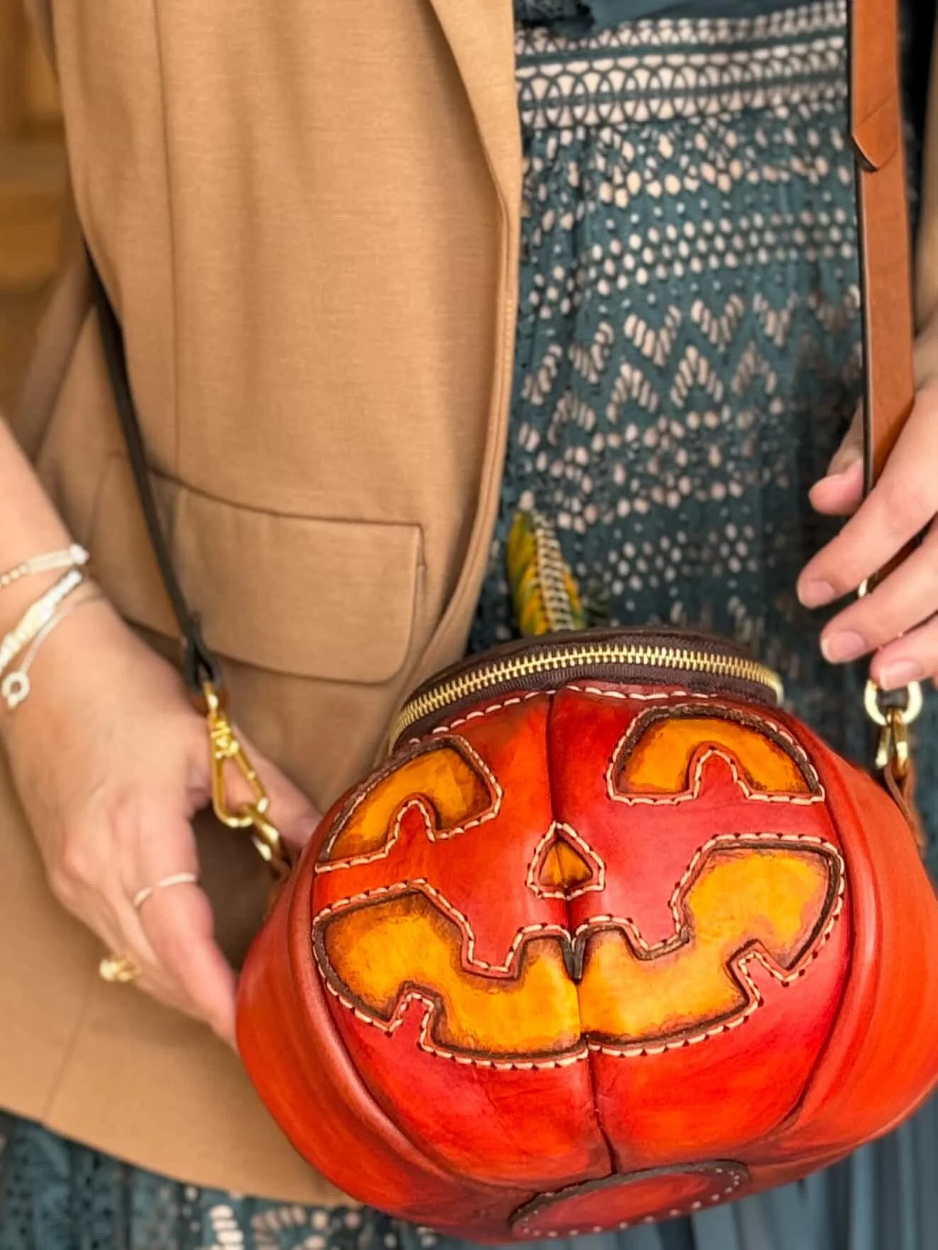 a customer submitted photo of her holding her Great Pumpkin bag against a tan jacket and teal and tan dress.