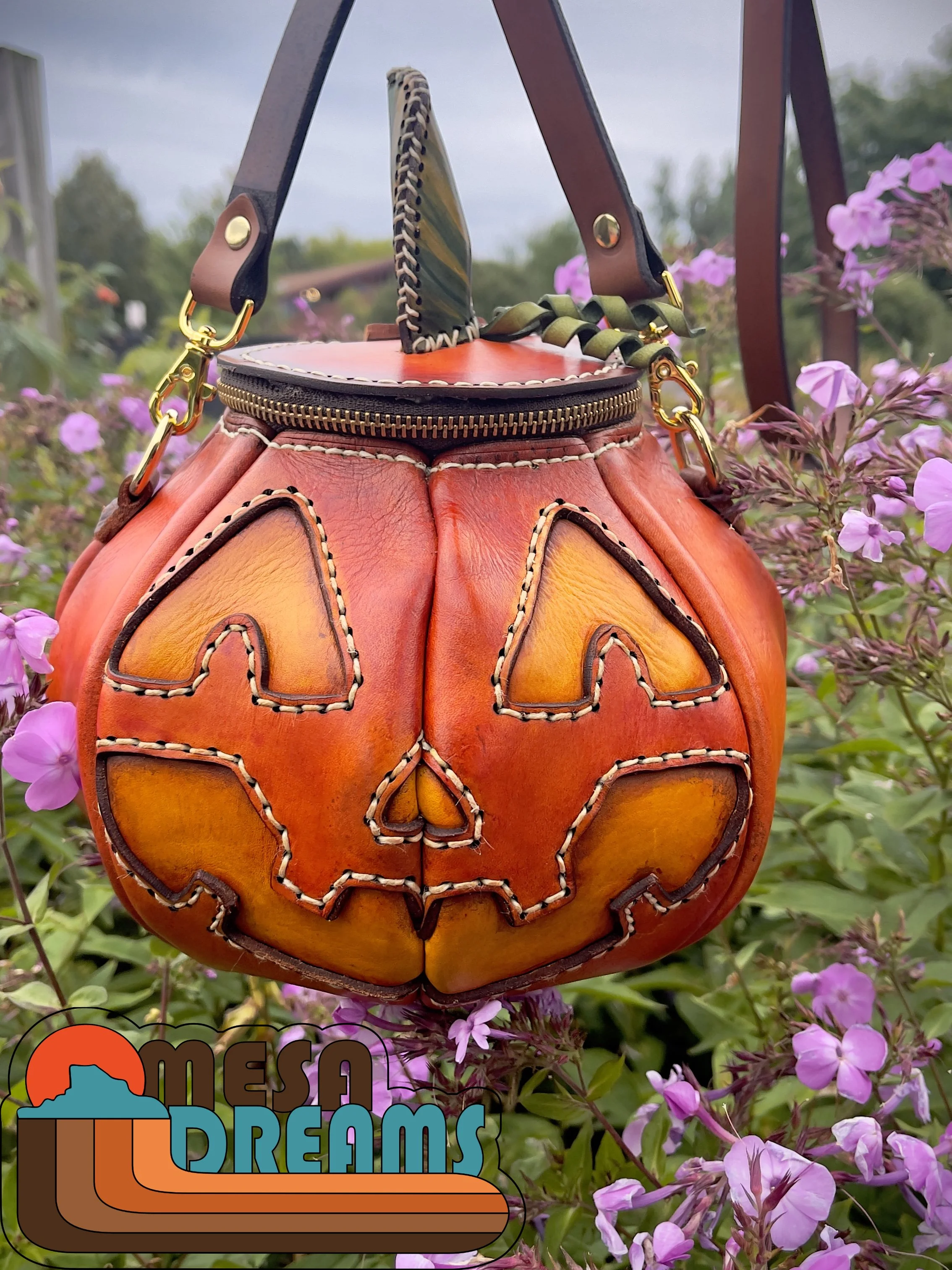 The Great Pumpkin leather bag hanging in a field of purple flowers
