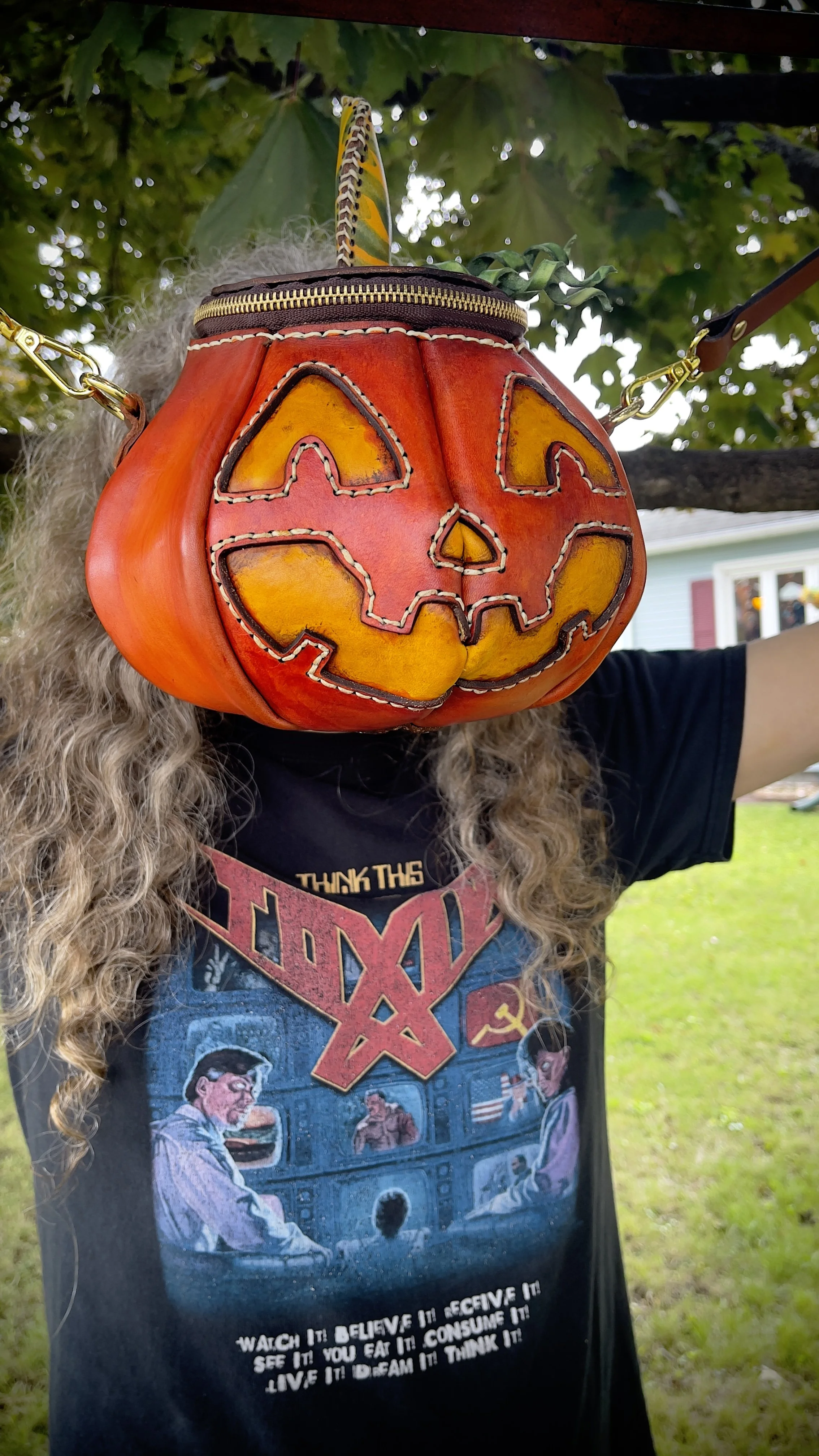 photo of a handmade leather pumpkin bag with a jack-o-lantern face being help up in front of Djerek’s face, Brandy’s husband.