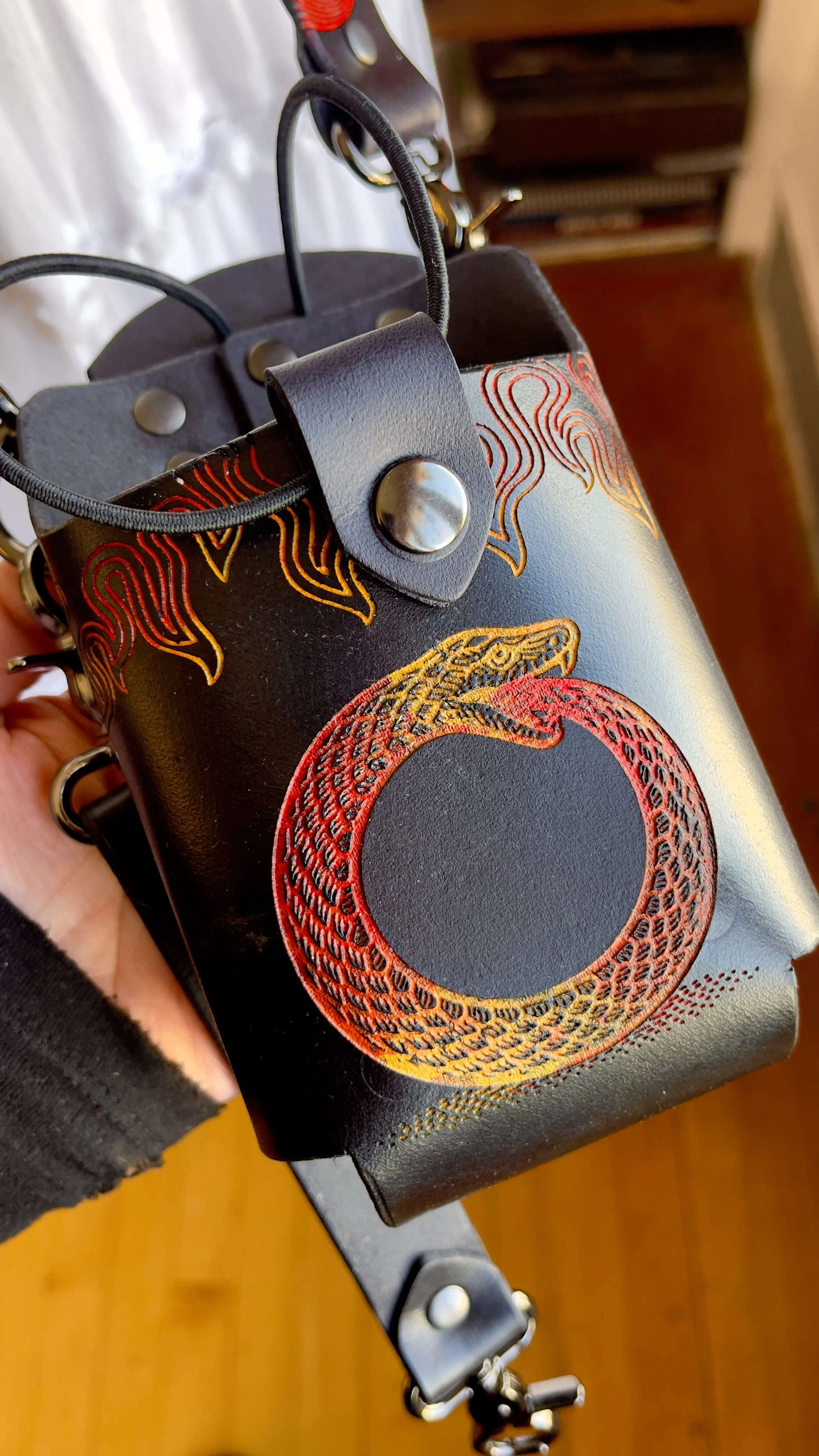 a black leather fire radio holster bucket adorned with an ouroboros snake and flames painted in red, yellow and oranges