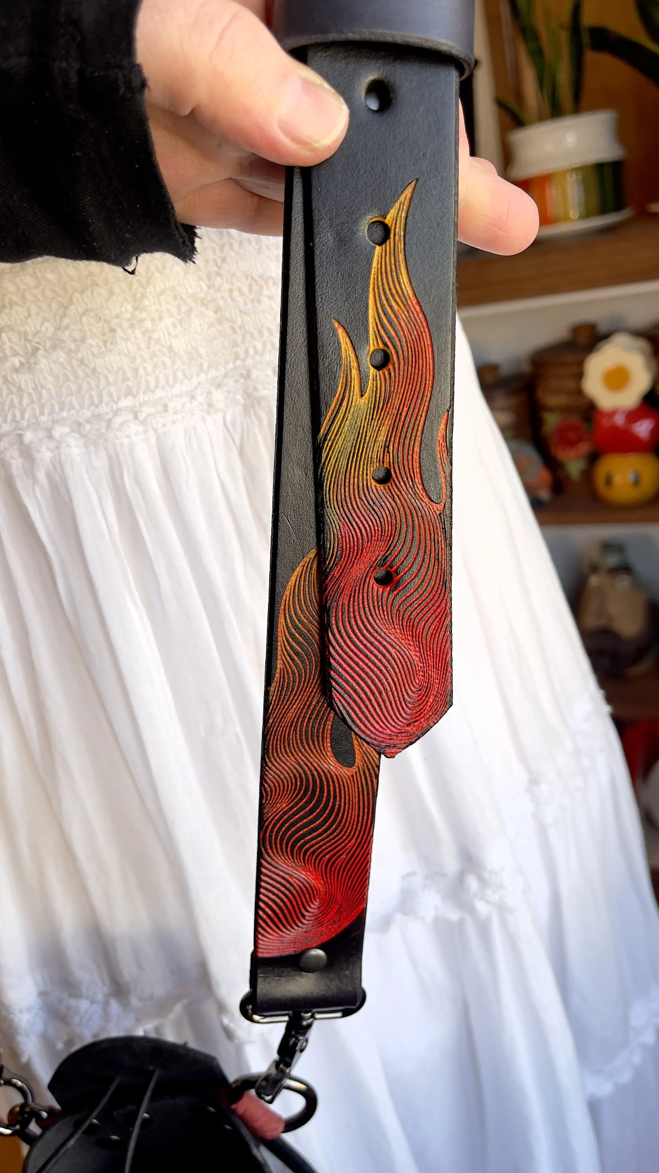 A black leather fire radio strap showing the ends covered in engraved flames and fire. They are painted in bold red, orange and yellow tones.