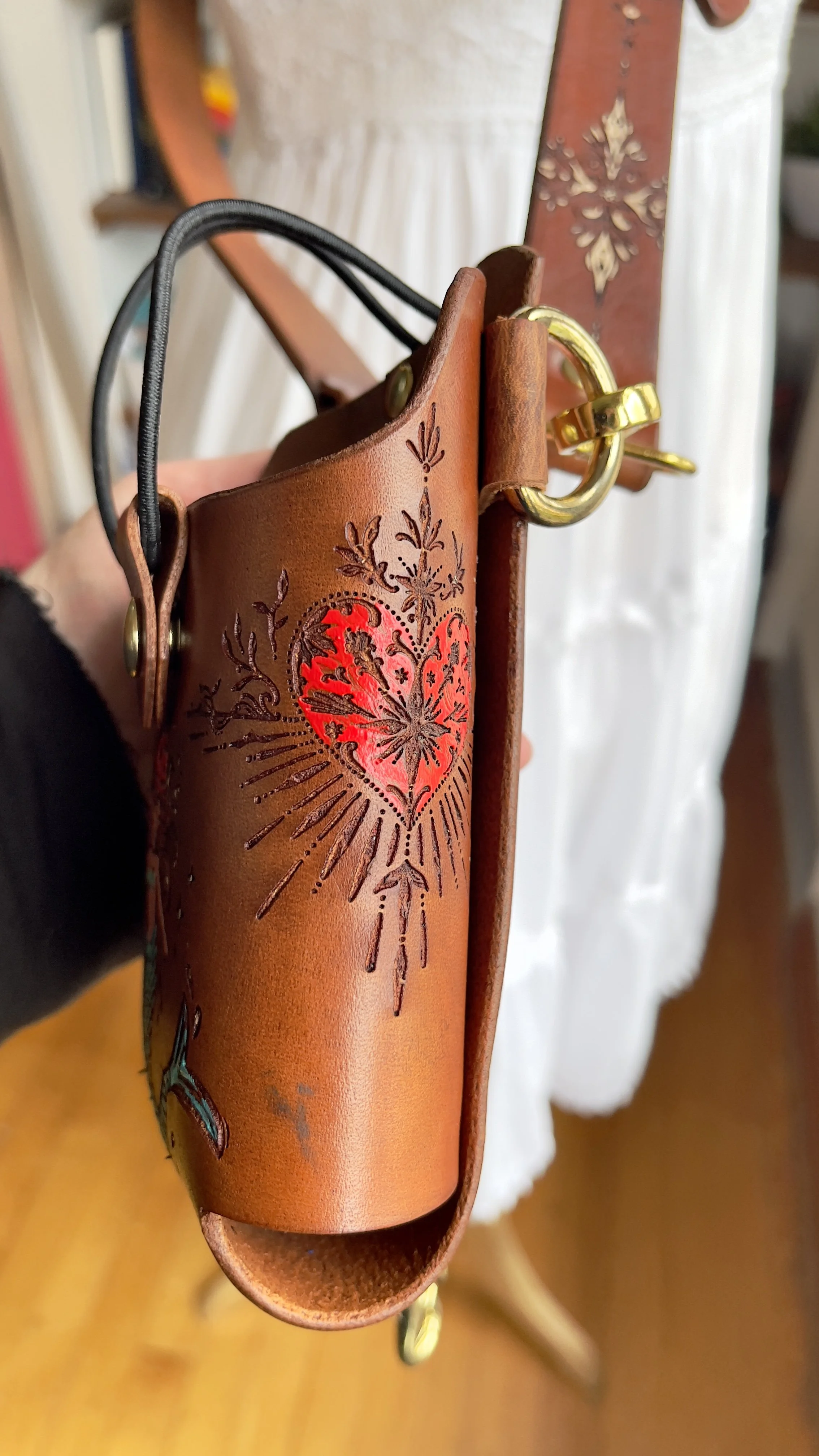 a brown leather fire radio holster with a sacred heart engraved and hand painted on the side panel