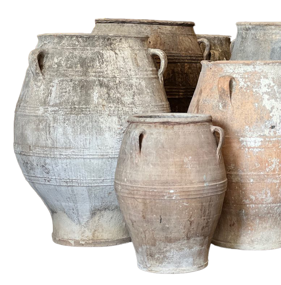 Group of large, weathered clay or ceramic jars with handles, arranged close together against a dark background.