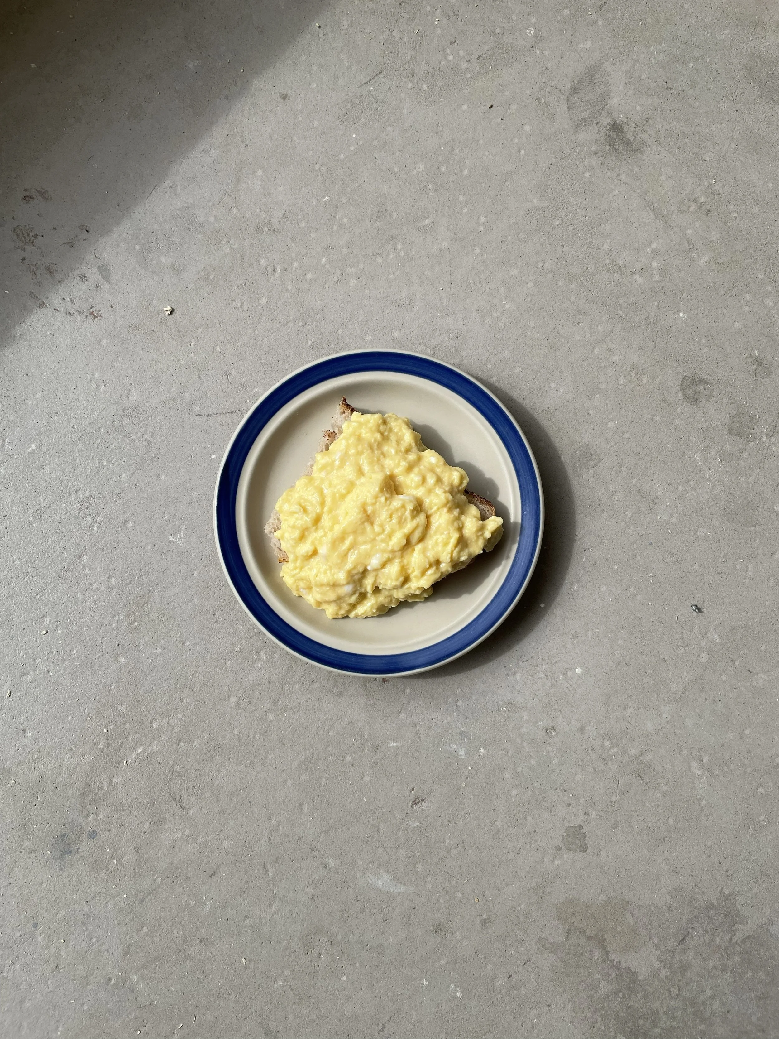 A plate of scrambled eggs on a gray concrete surface.
