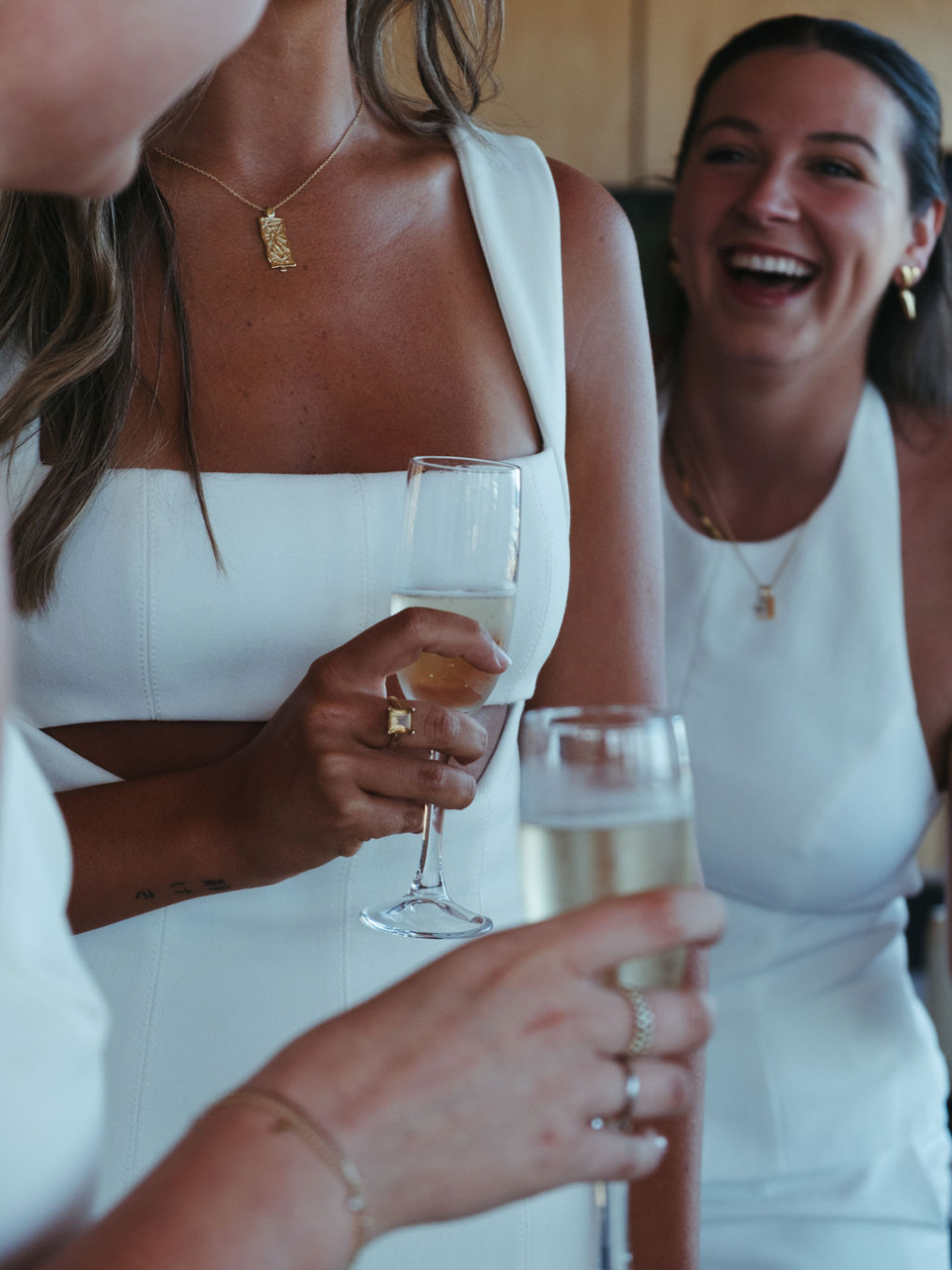 Women in white dresses celebrating with champagne glasses, smiling and enjoying a social gathering.