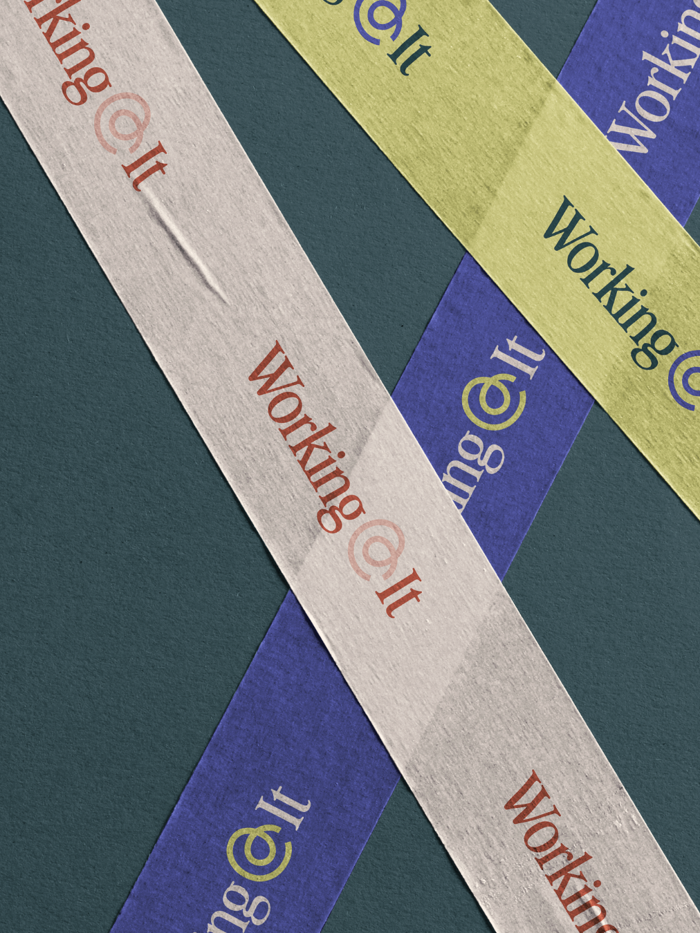 Colorful strips of paper with the words 'Working@it' printed on them, overlapping each other on a teal background.