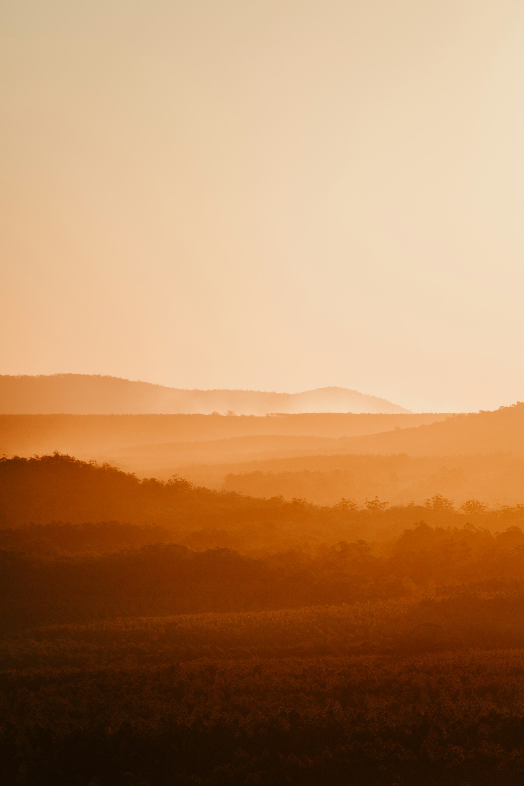 Sunset over a landscape of rolling hills and trees in the distance, with a warm, orange hue.