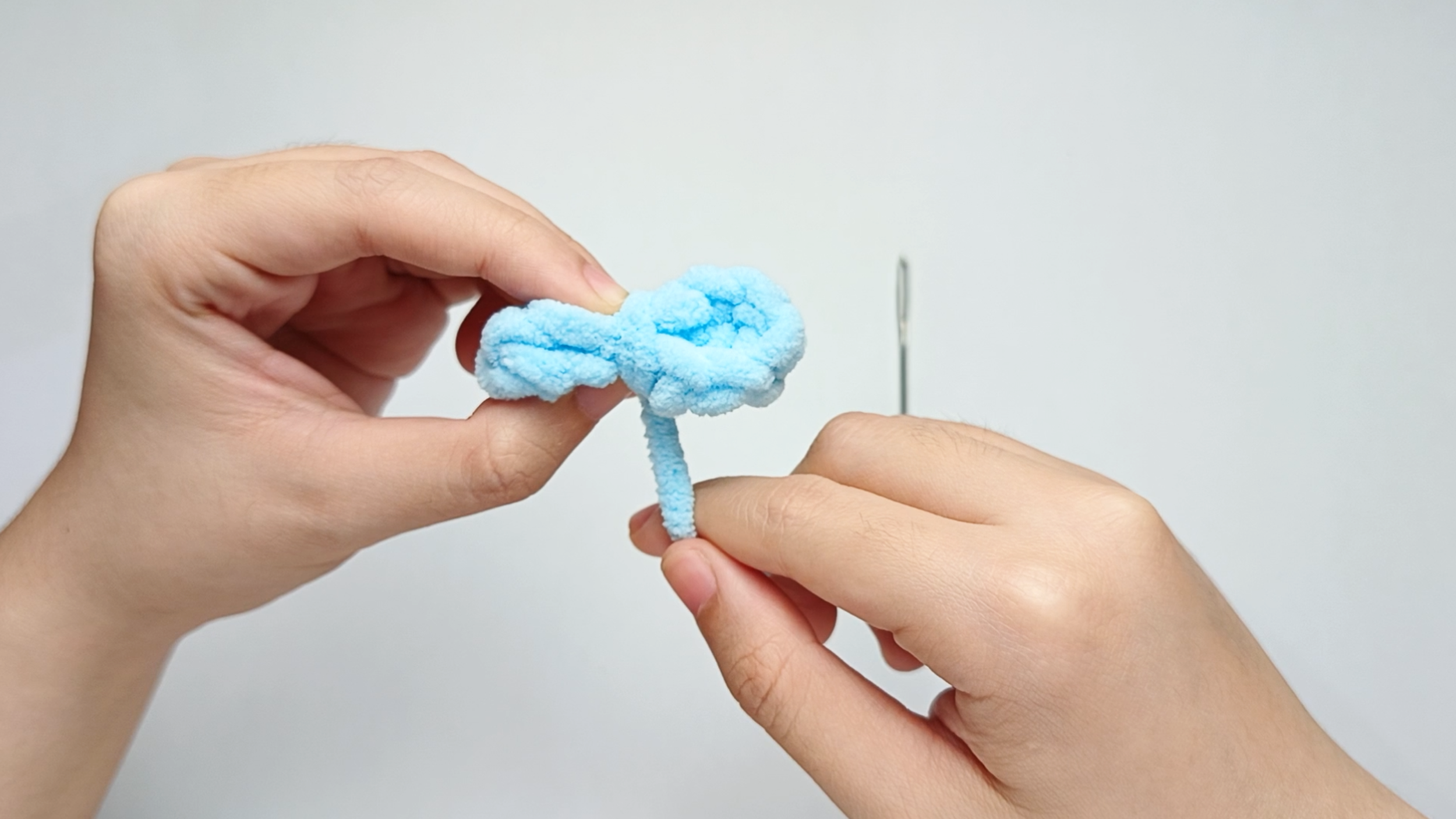 Wrap the center: Pinch the middle of the two loops together, then wrap the yarn tail around that center 3 times.