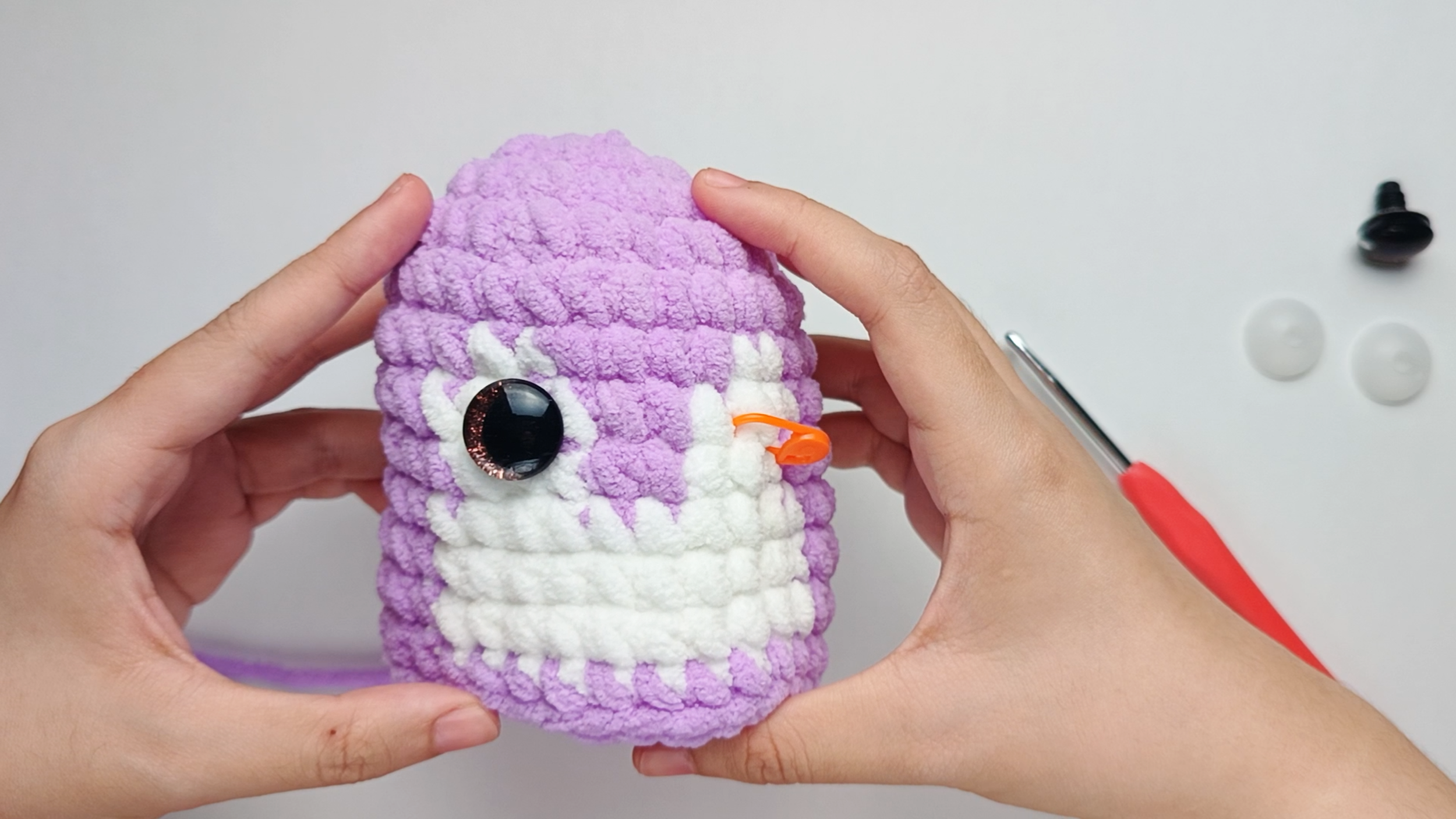 Place the first eye: Remove the stitch marker. With the right side of your piece facing you, push the first eye's stem between two stitches. The side with colored fabric should face outward.