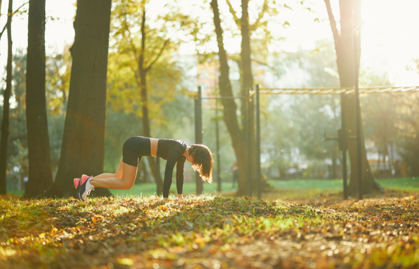 Frau macht im Park im Sonnenschein Liegestütze auf dem Boden.