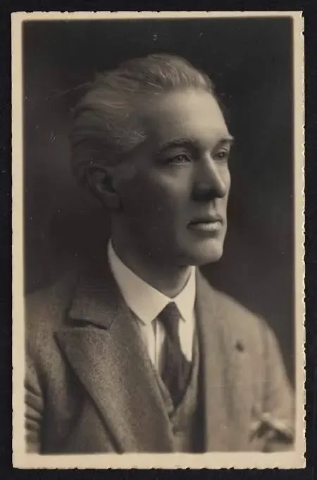 A vintage black-and-white portrait of a young man with neatly combed hair, wearing a suit and tie, looking to the side.