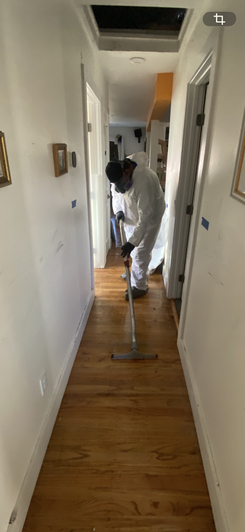 Person in protective suit and mask cleaning hardwood floor with a mop in a hallway.