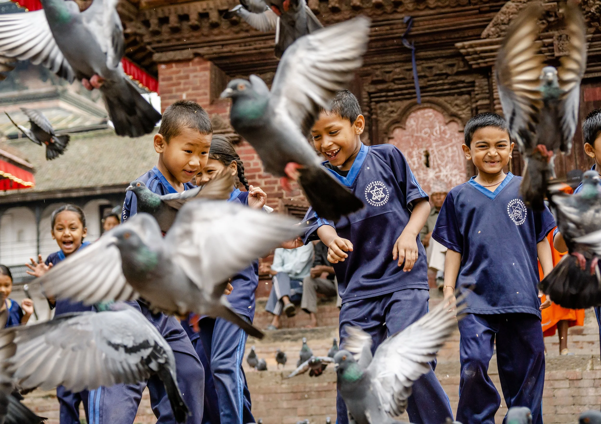 Children in navy blue uniforms feeding pigeons outdoors.