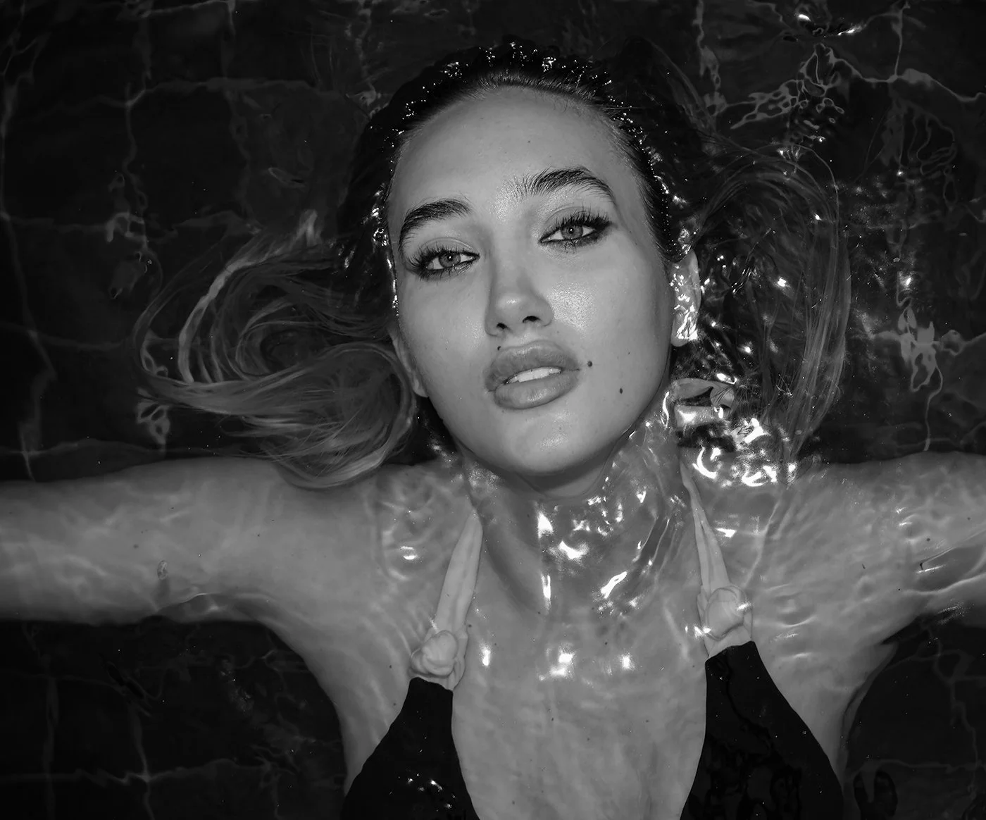A woman with wet hair floating in water, gazing at the camera in black and white.