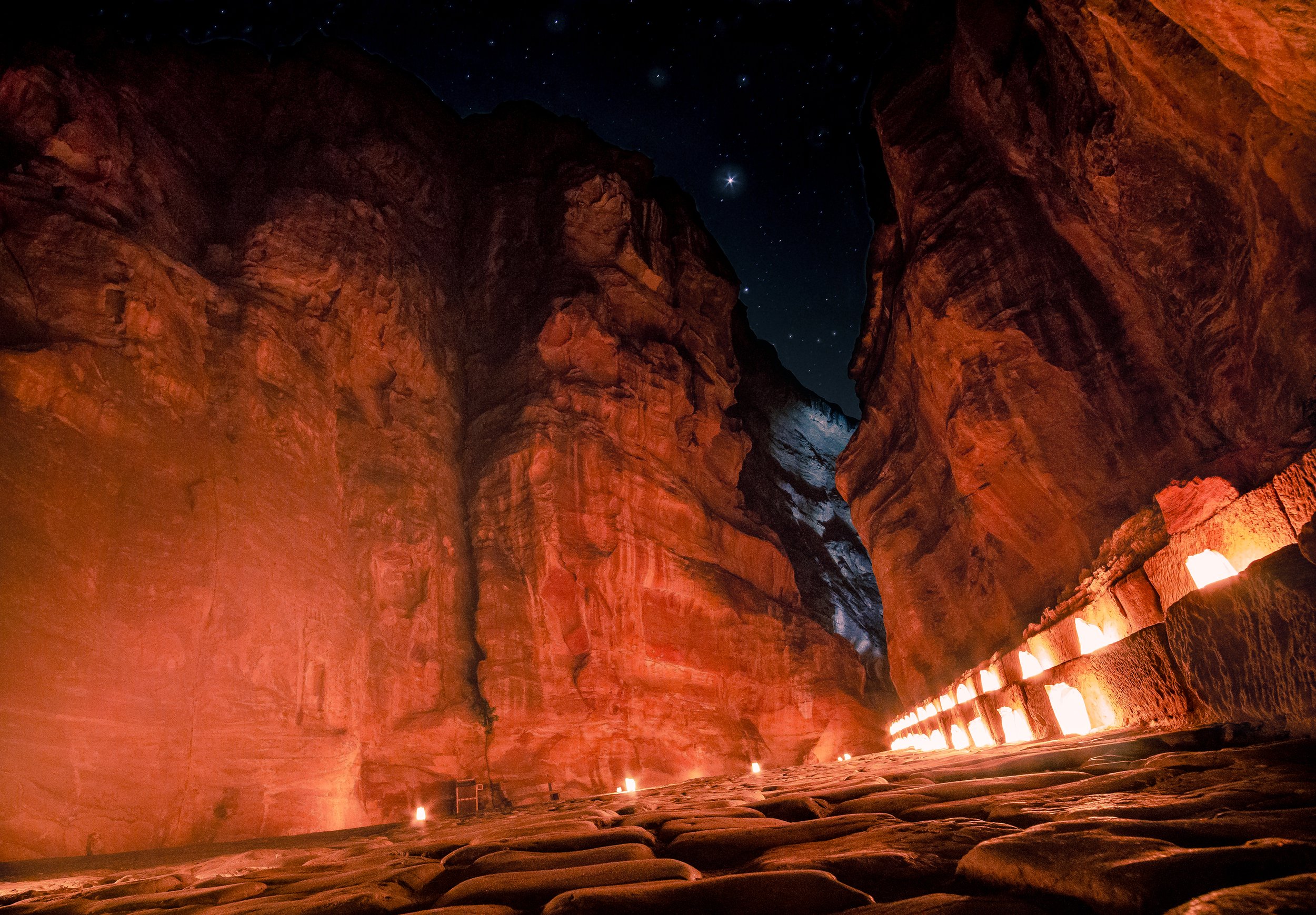Inside a canyon or cave with tall rock walls illuminated by warm-colored lighting, and a starry night sky visible through an opening at the top.