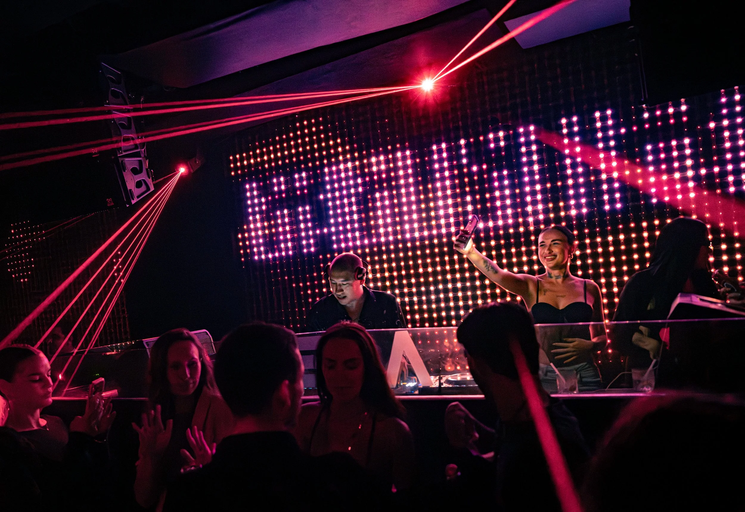 People dancing and enjoying a nightclub with laser lights and LED display.