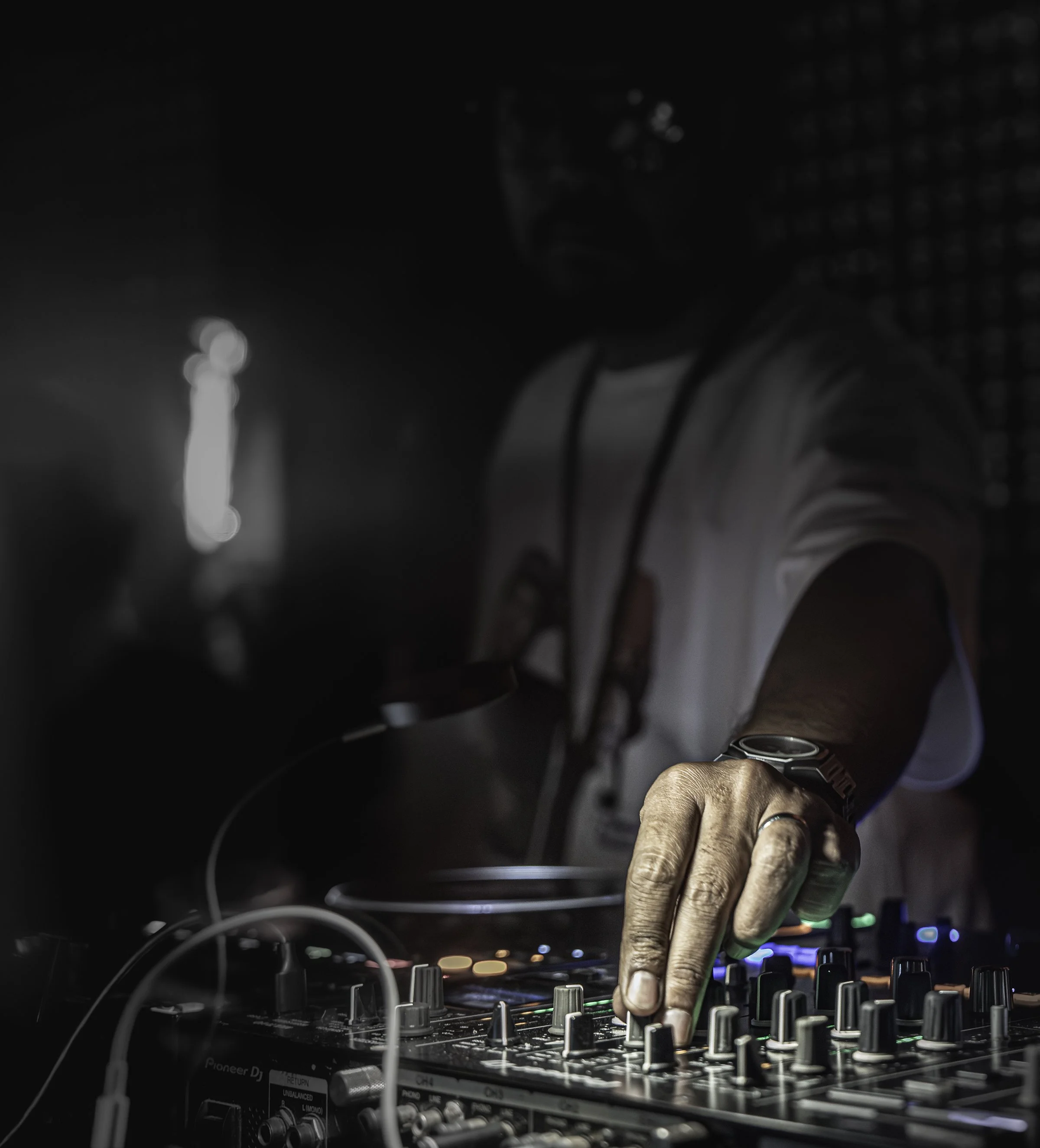 DJ mixing music at a nightclub, close-up of hands adjusting controls on a DJ mixer with colorful lights in the background.