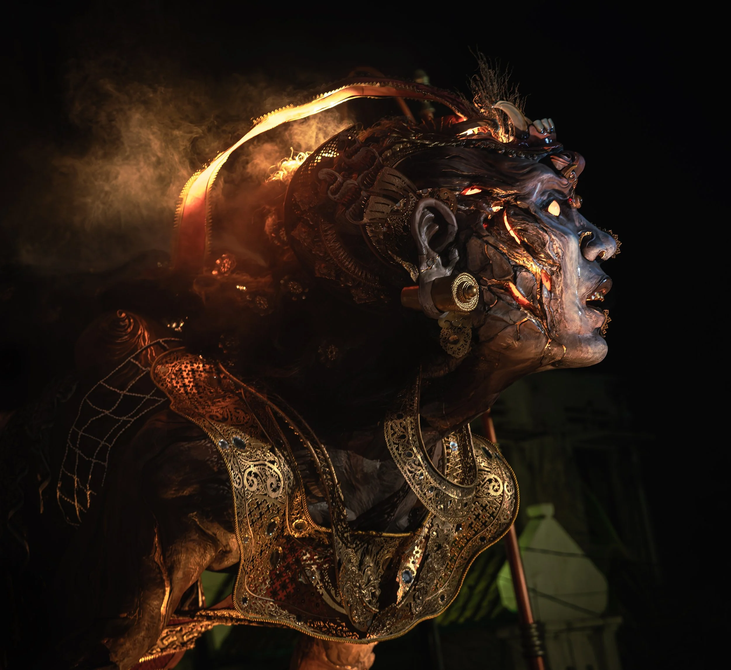 A detailed metallic sculpture of a face with intricate and ornate designs illuminated against a dark background.