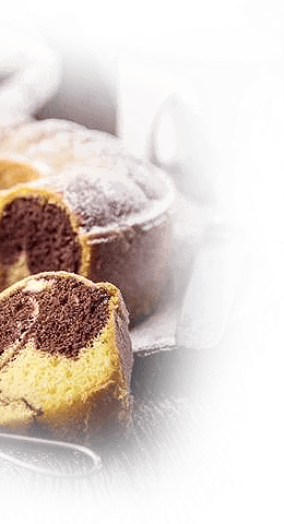 A variety of baked goods, including chocolate and lemon pound cakes, displayed on a glass tray next to a cup of black coffee on a dark surface.
