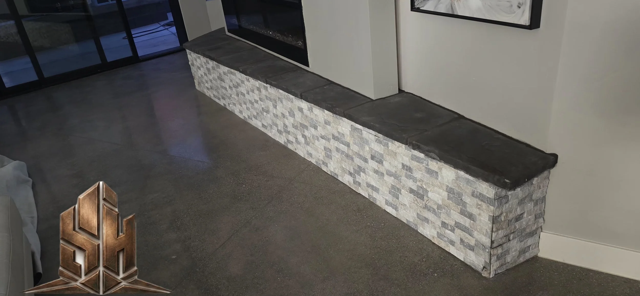 A modern interior corner with a stone and brick fireplace or feature wall, a concrete floor, a window with black frames, and a light-colored wall.