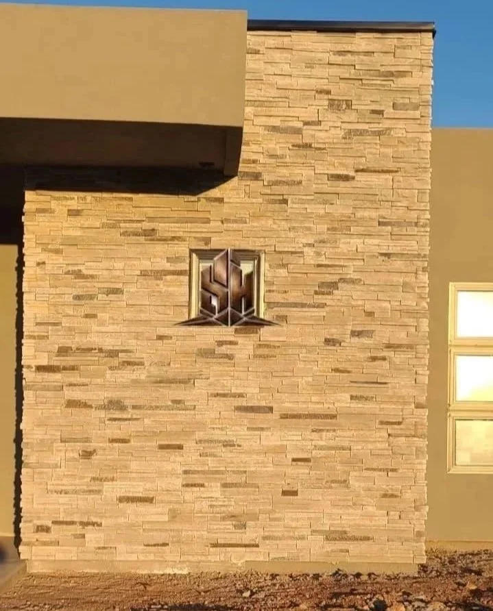 Exterior view of a modern house with an artificial stone facade, a small window with a decorative grille, and a section of a beige wall.