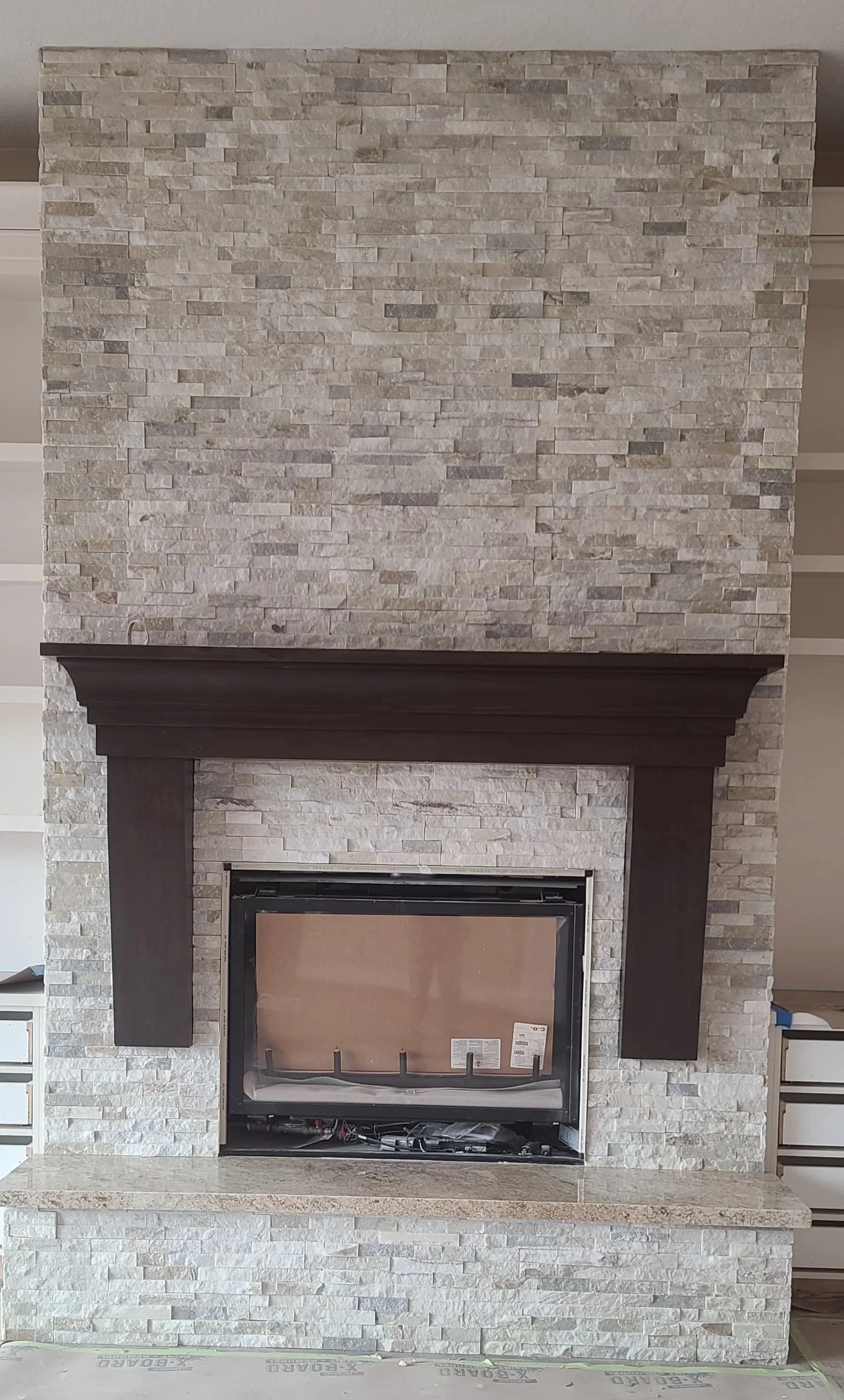 A fireplace with a natural stone facade, black mantel, and unfinished interior, surrounded by white shelving and wall with horizontal accents.