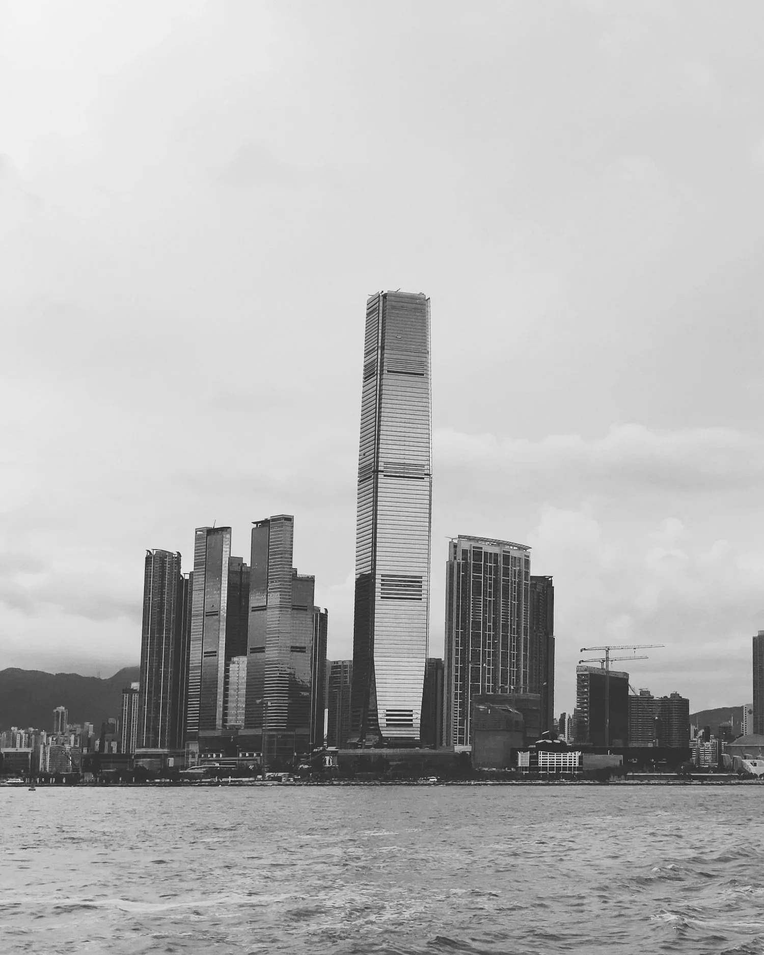 A black and white photograph of a city skyline with tall skyscrapers viewed from across a body of water.