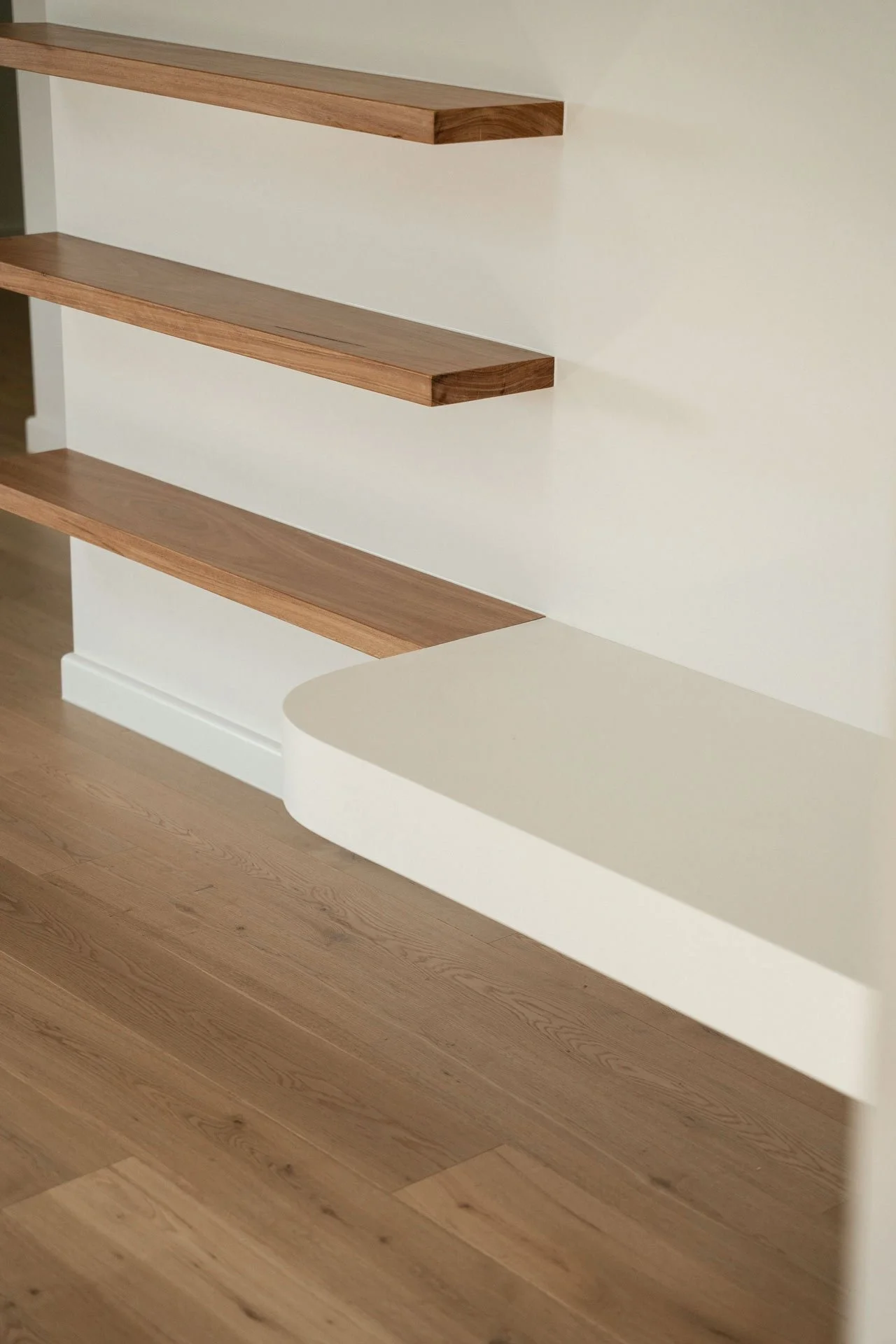 Close-up of wooden floating shelves mounted on a white wall and a section of wooden flooring.