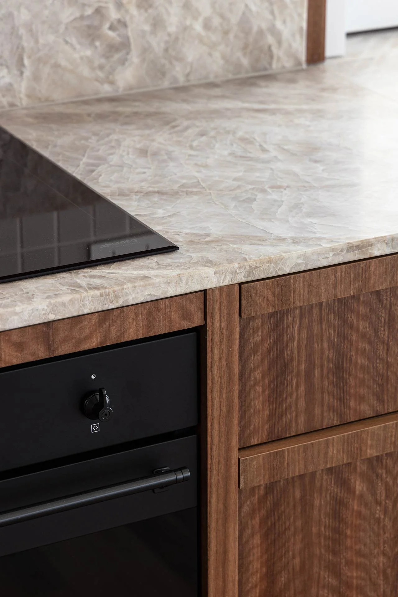 Close-up of a kitchen countertop with a stovetop, wooden cabinet doors, and a wall behind.