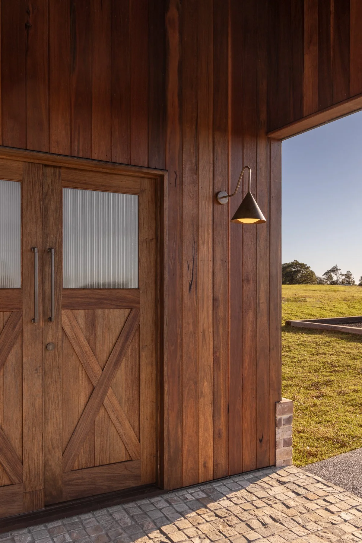 Wooden barn door with frosted glass panels, a rustic wall sconce, and a view of a grassy field and trees outside.